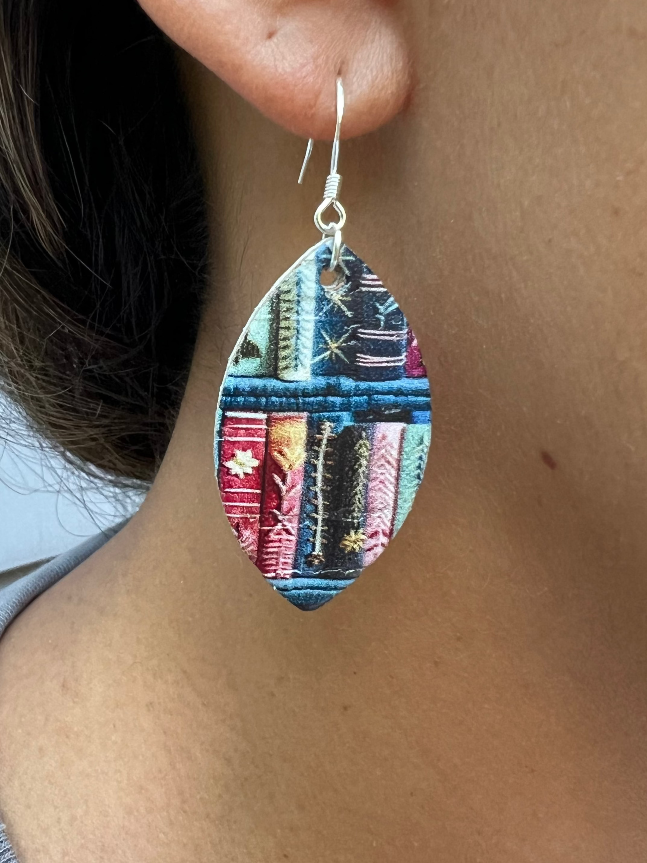 Close-up of a person wearing colorful earrings with a book pattern.