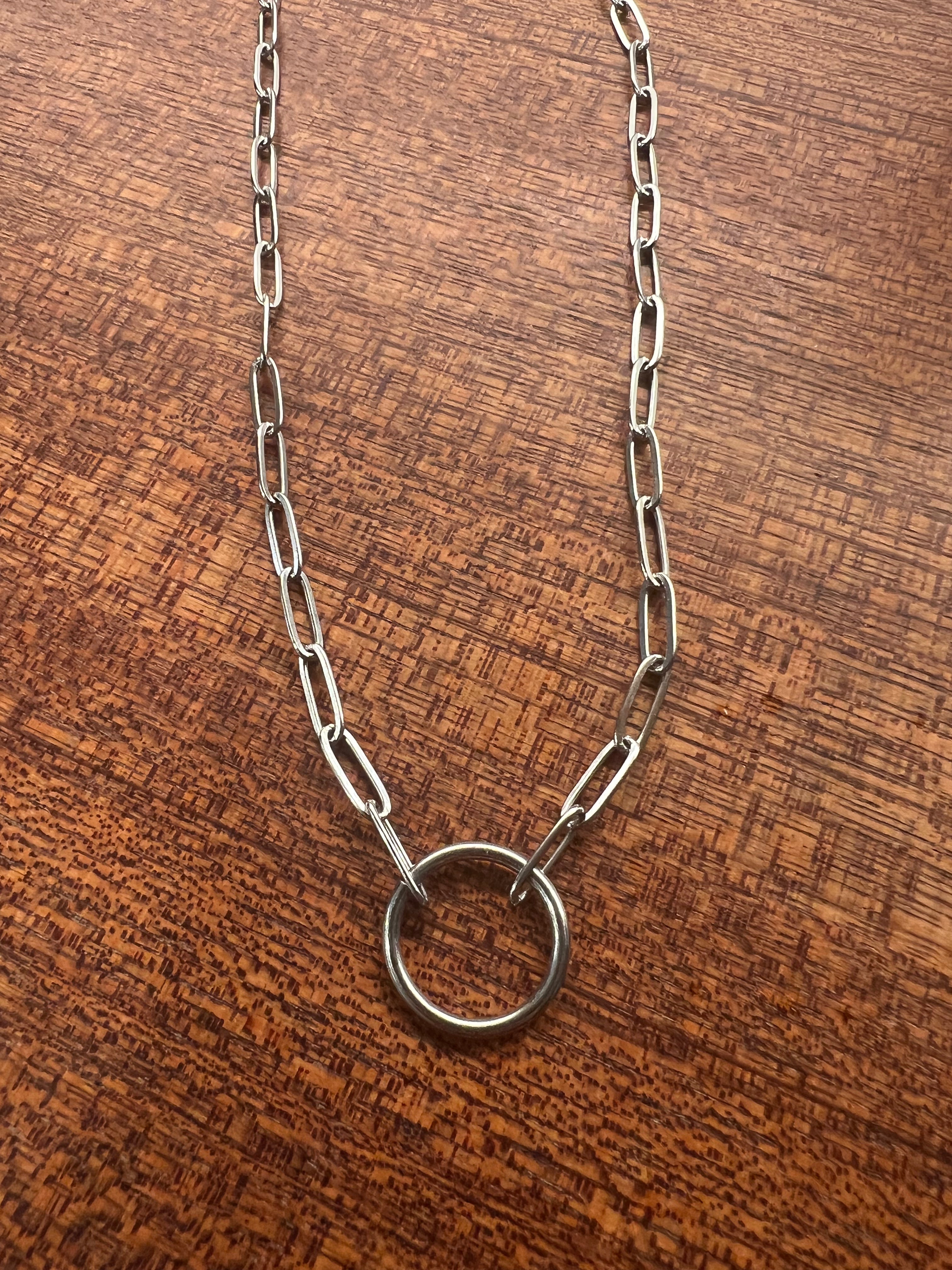 Silver chain necklace with a round ring pendant on a wooden surface