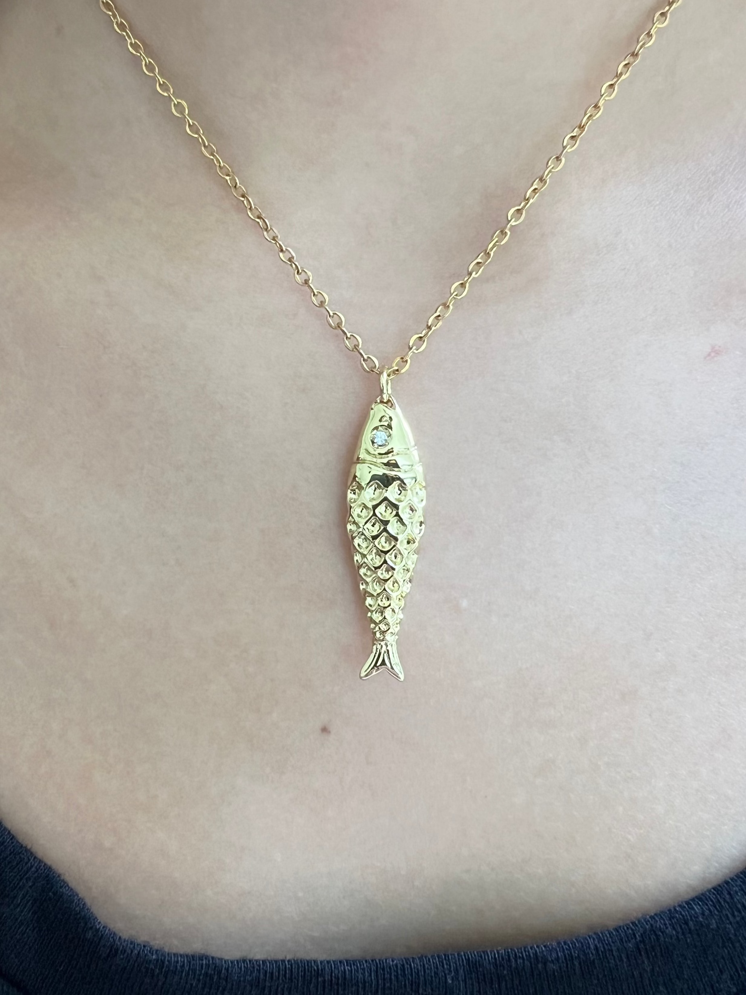 Gold fish-shaped pendant necklace on a person's neck