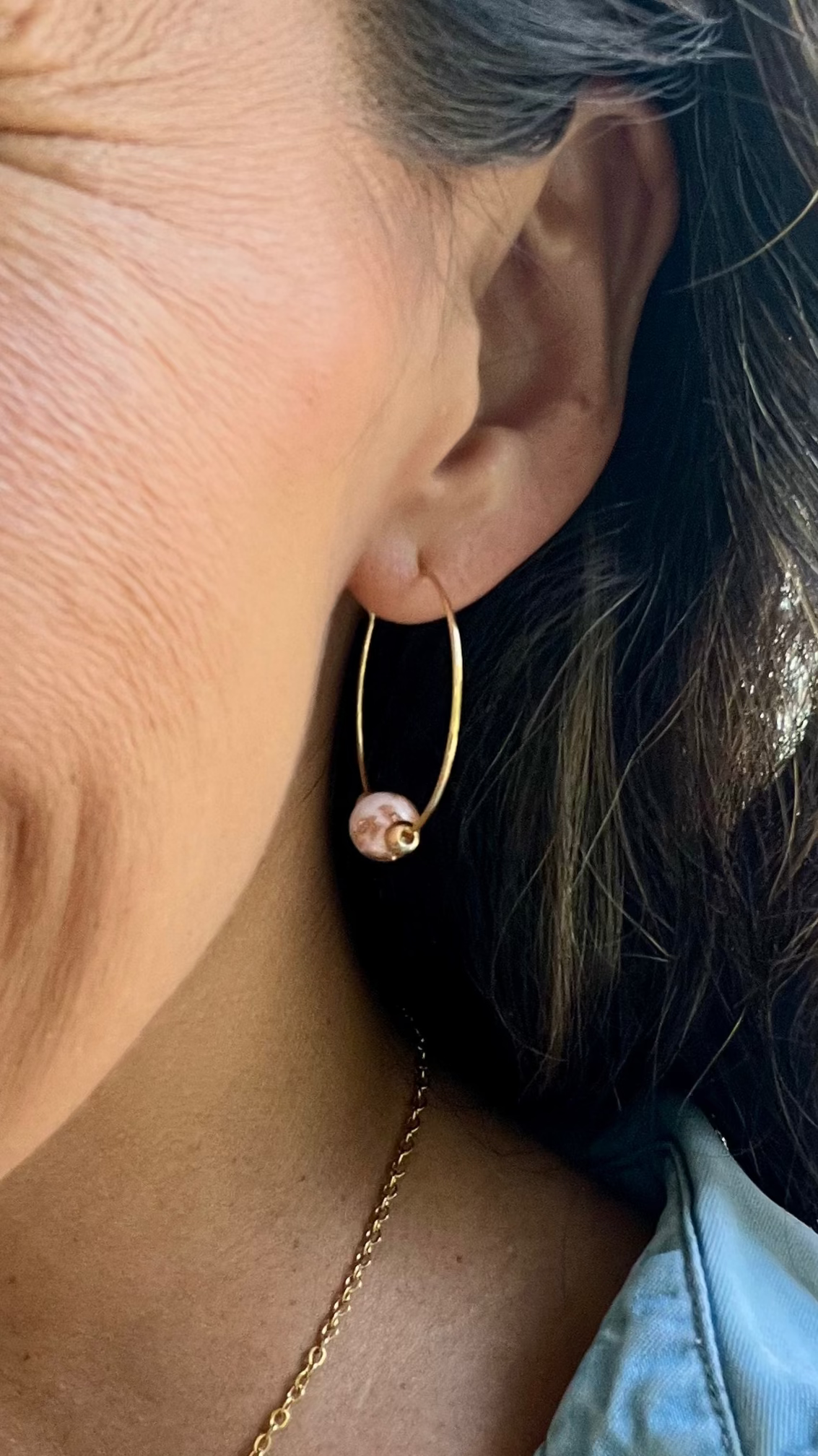 Close-up of an ear wearing a gold hoop earring with a pink pearl.