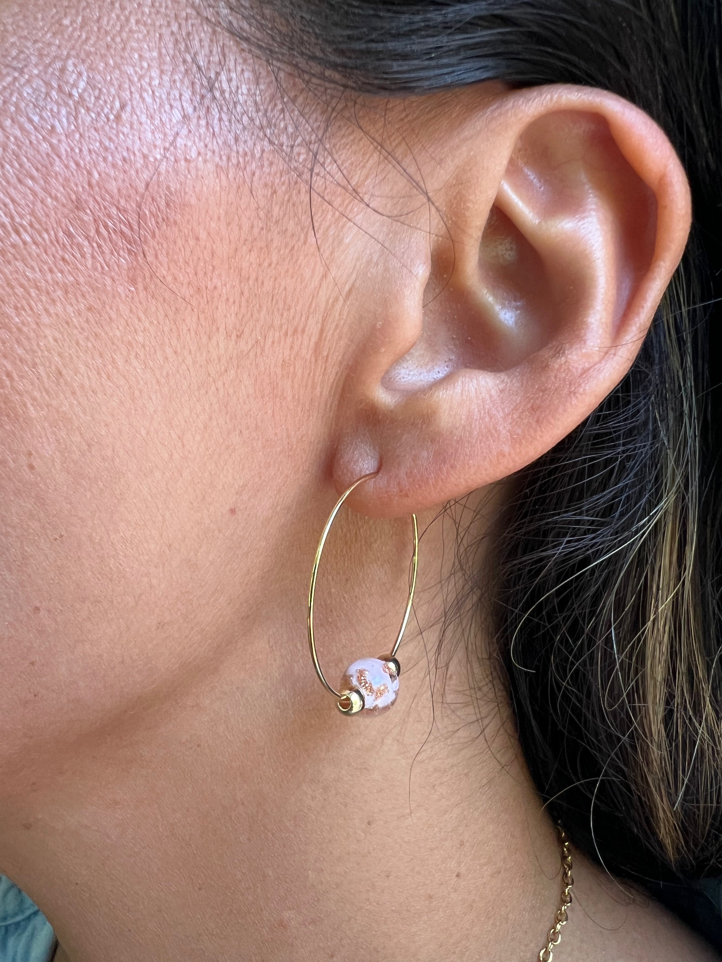 Close-up of an ear wearing a gold hoop earring with a pink bead.