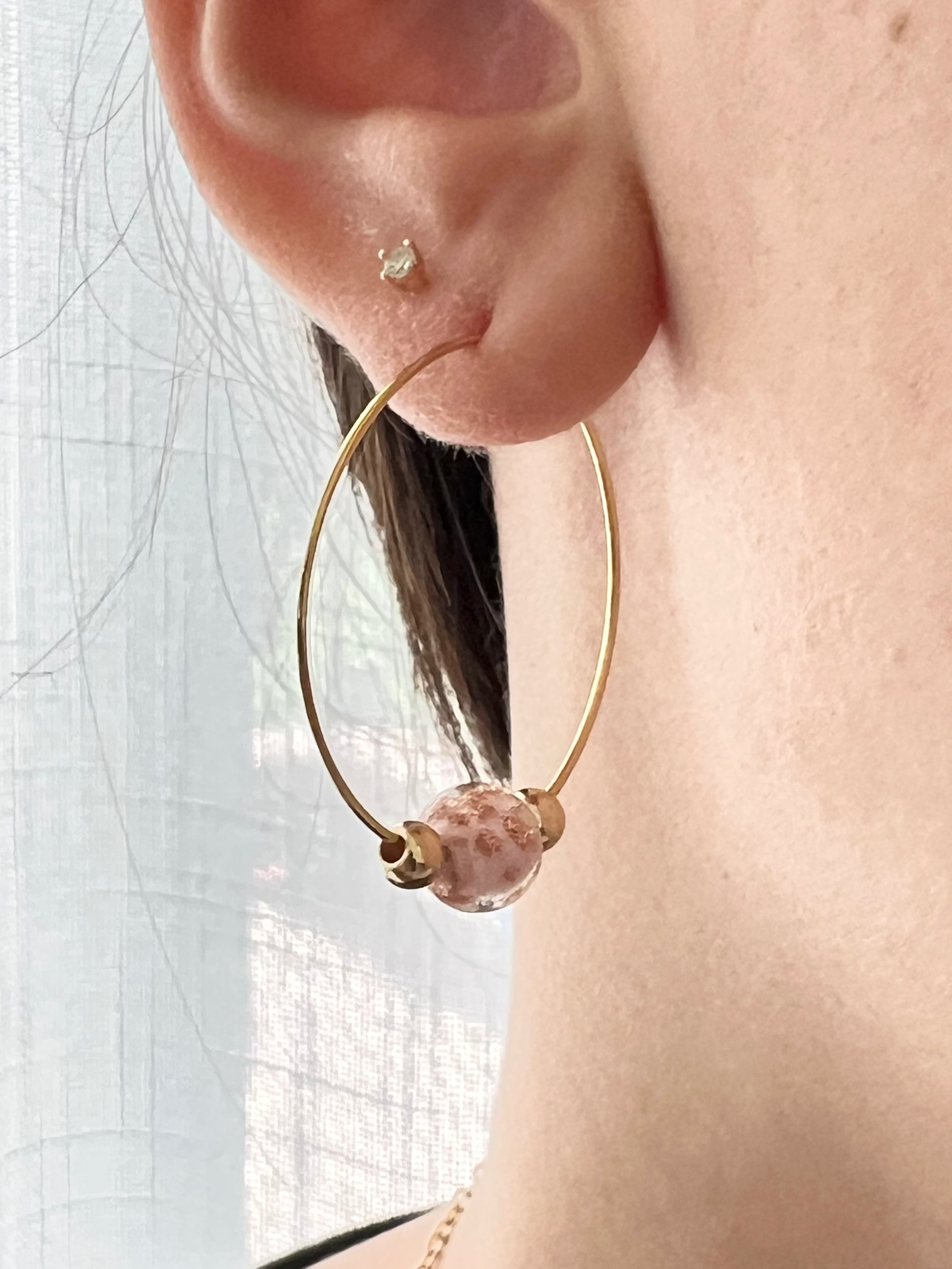 Close-up of an ear wearing a gold hoop earring with a pink gemstone.
