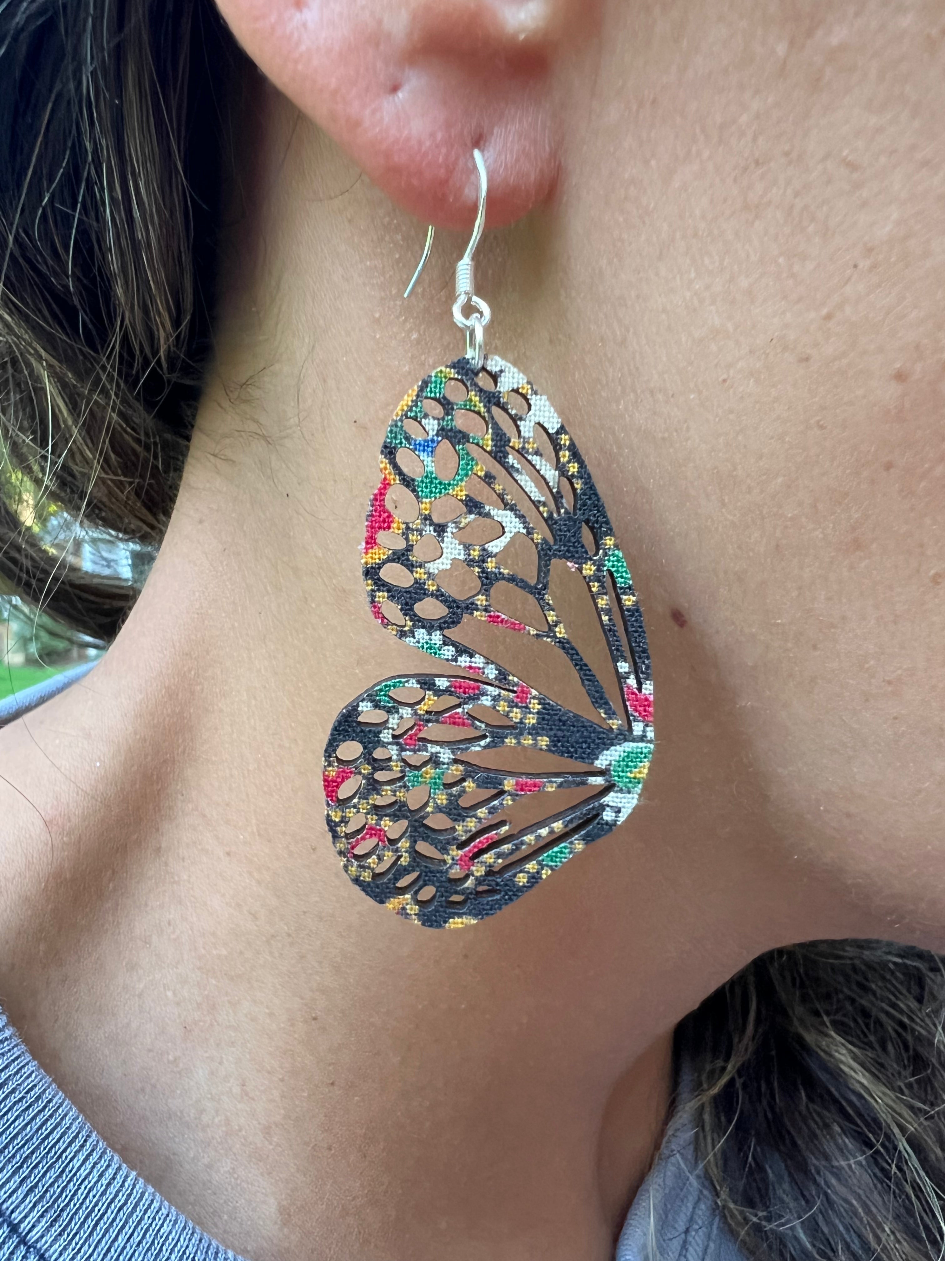 Butterfly-shaped earrings with a colorful pattern worn by a person.