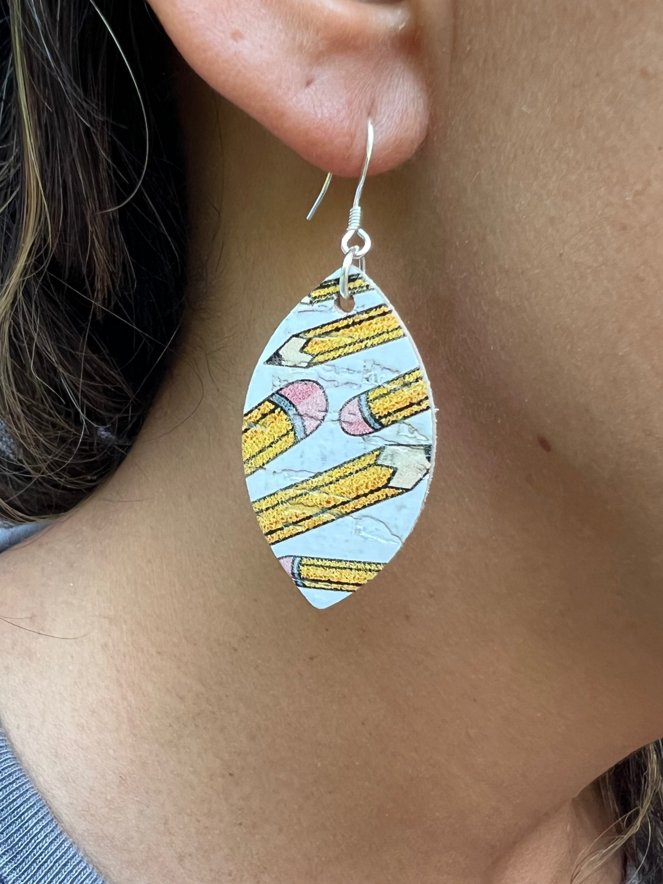Close-up of a person wearing colorful earrings with a pattern of pencils.