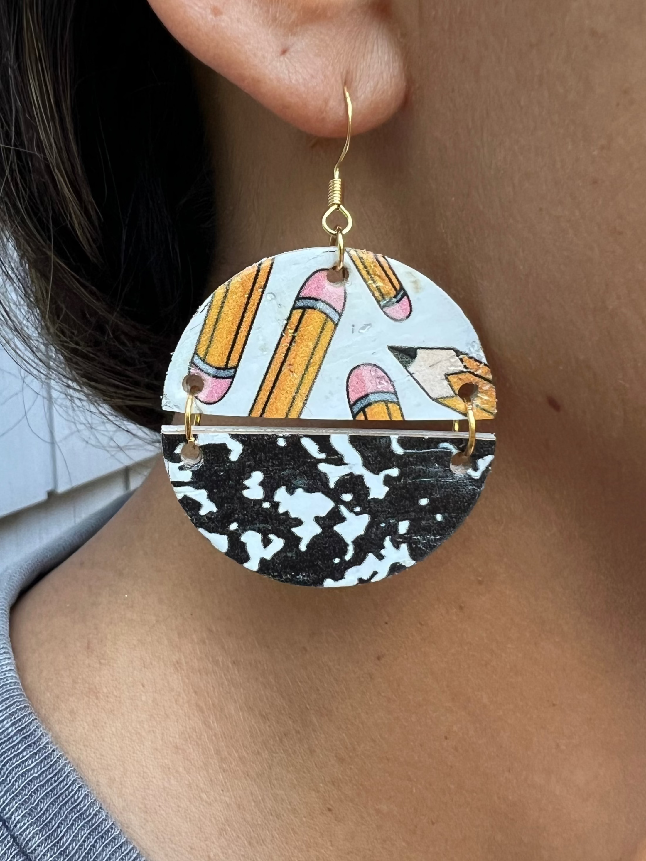 Close-up of an ear wearing a round earring with a pencil & design.