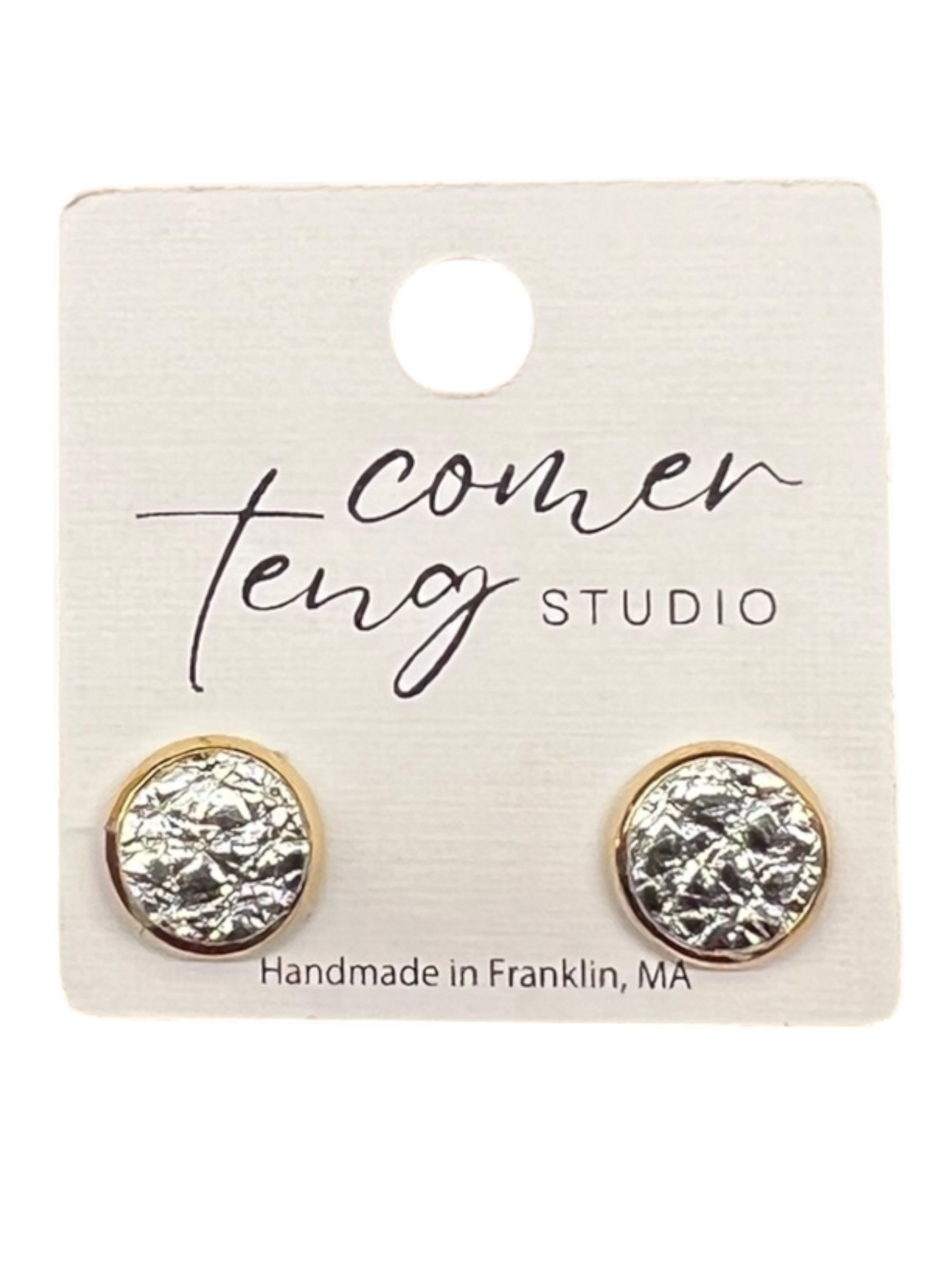 Pair of gold and silver stud earrings on a Comer Teeng Studio card.