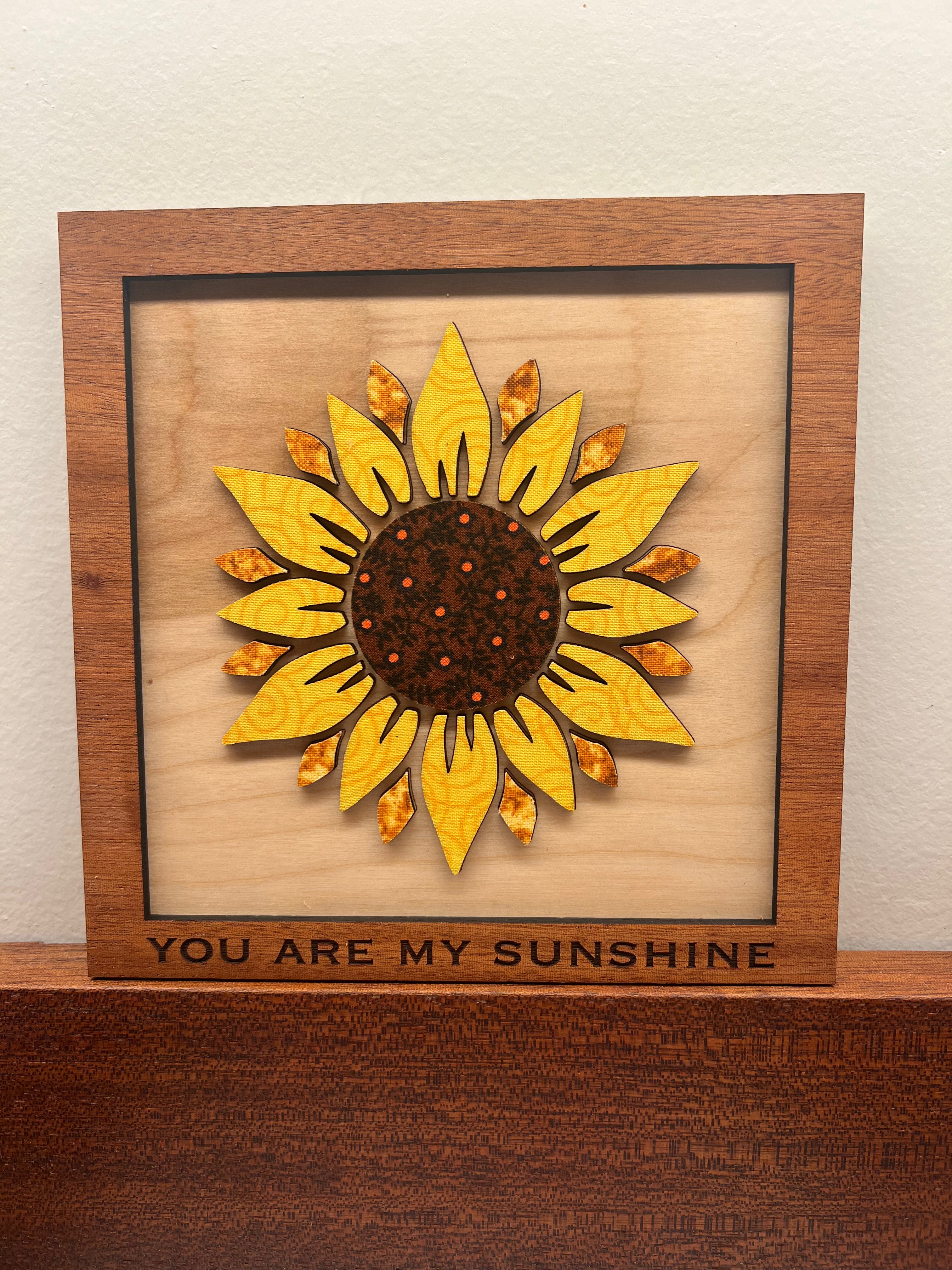 Wooden framed sunflower design with 'You Are My Sunshine' text on a wooden surface.