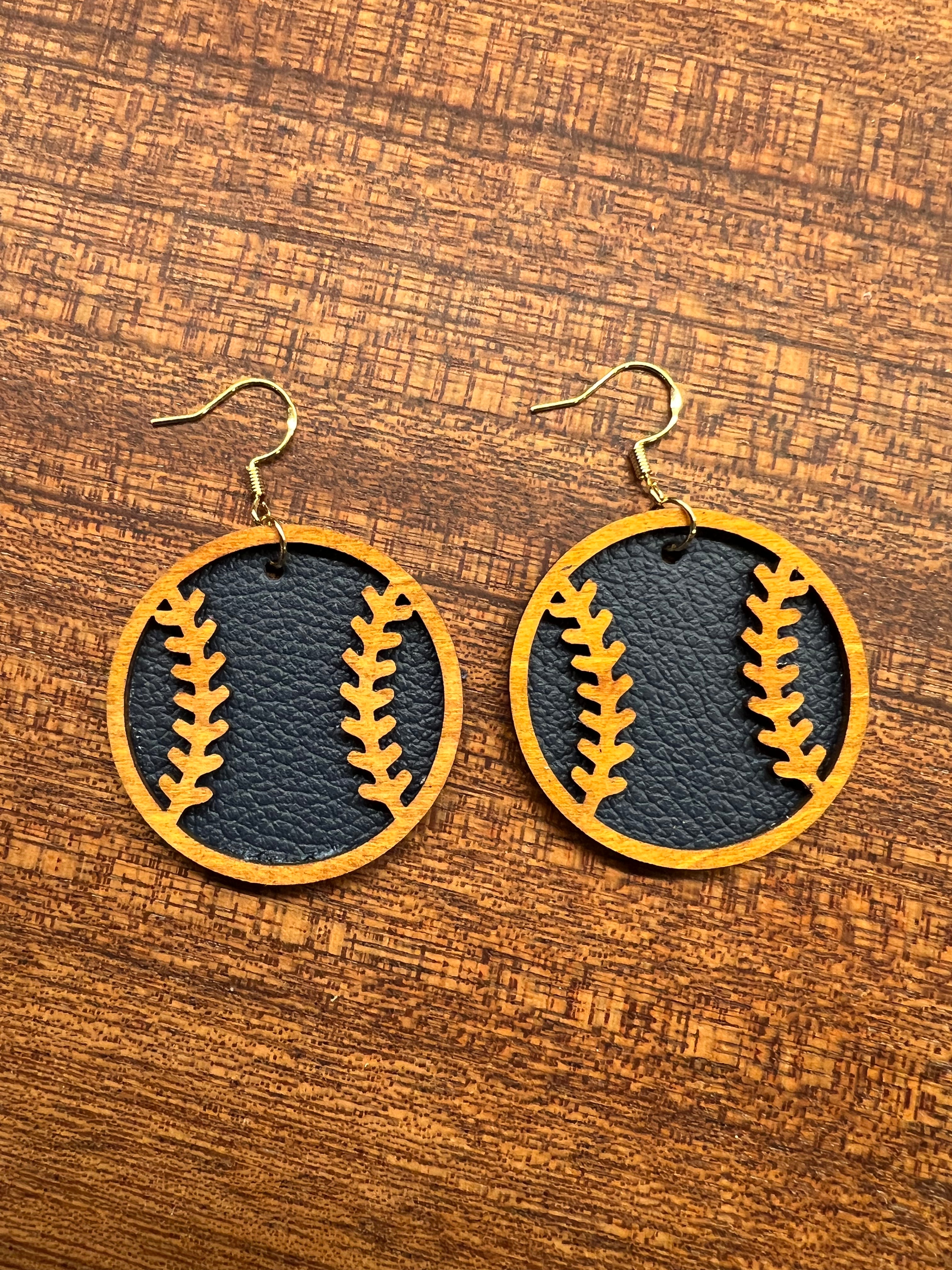 Baseball-shaped earrings with gold stitching on a wooden surface
