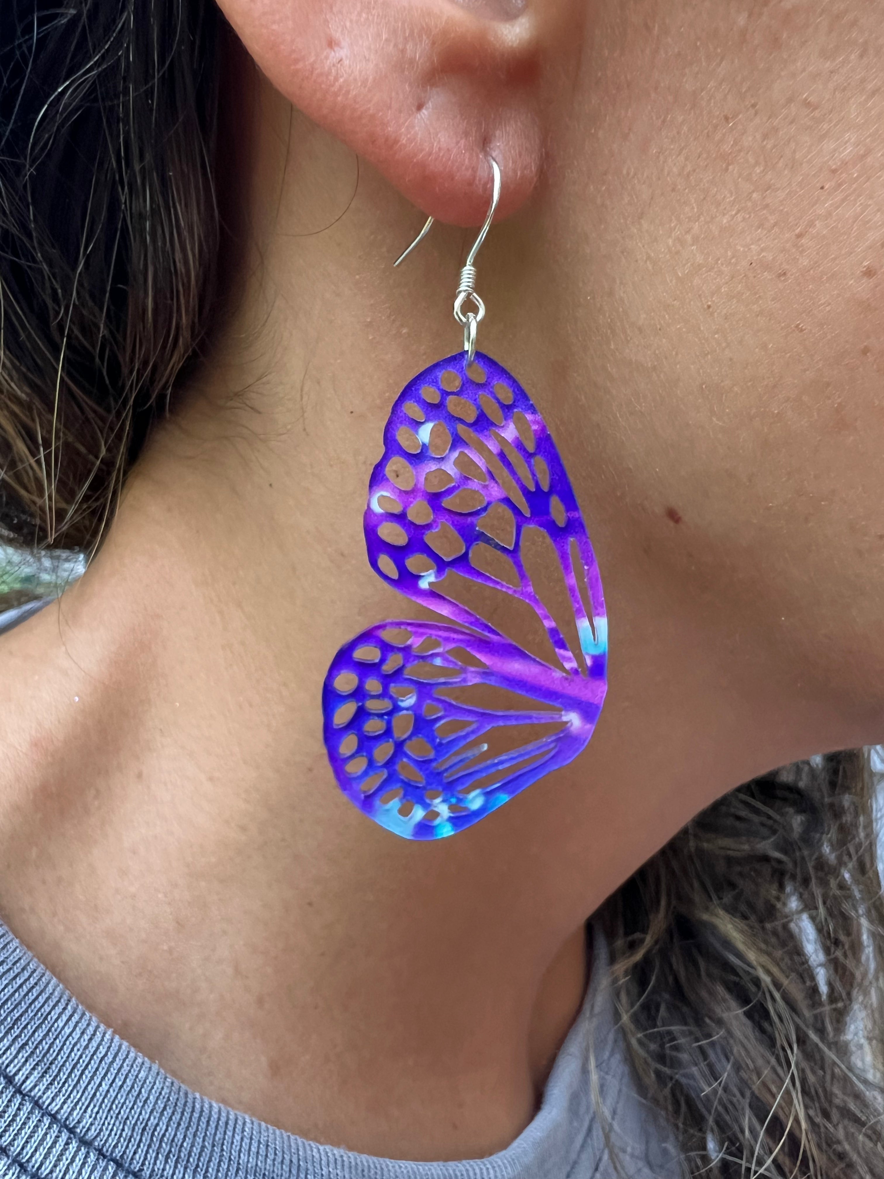 Butterfly-shaped earrings with a metallic sheen worn by a person.