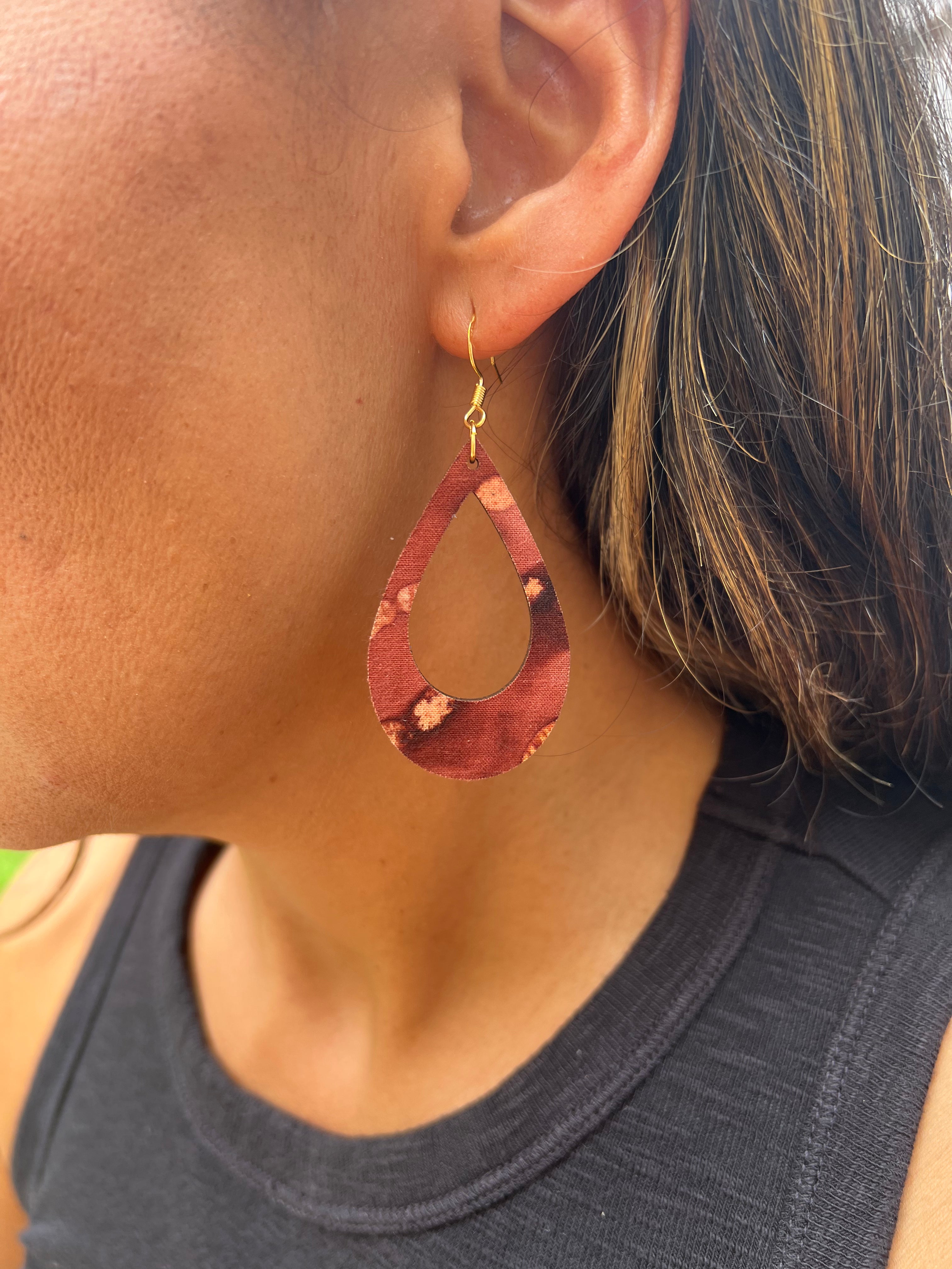Close-up of a person wearing a maroon teardrop earring with gold hook.