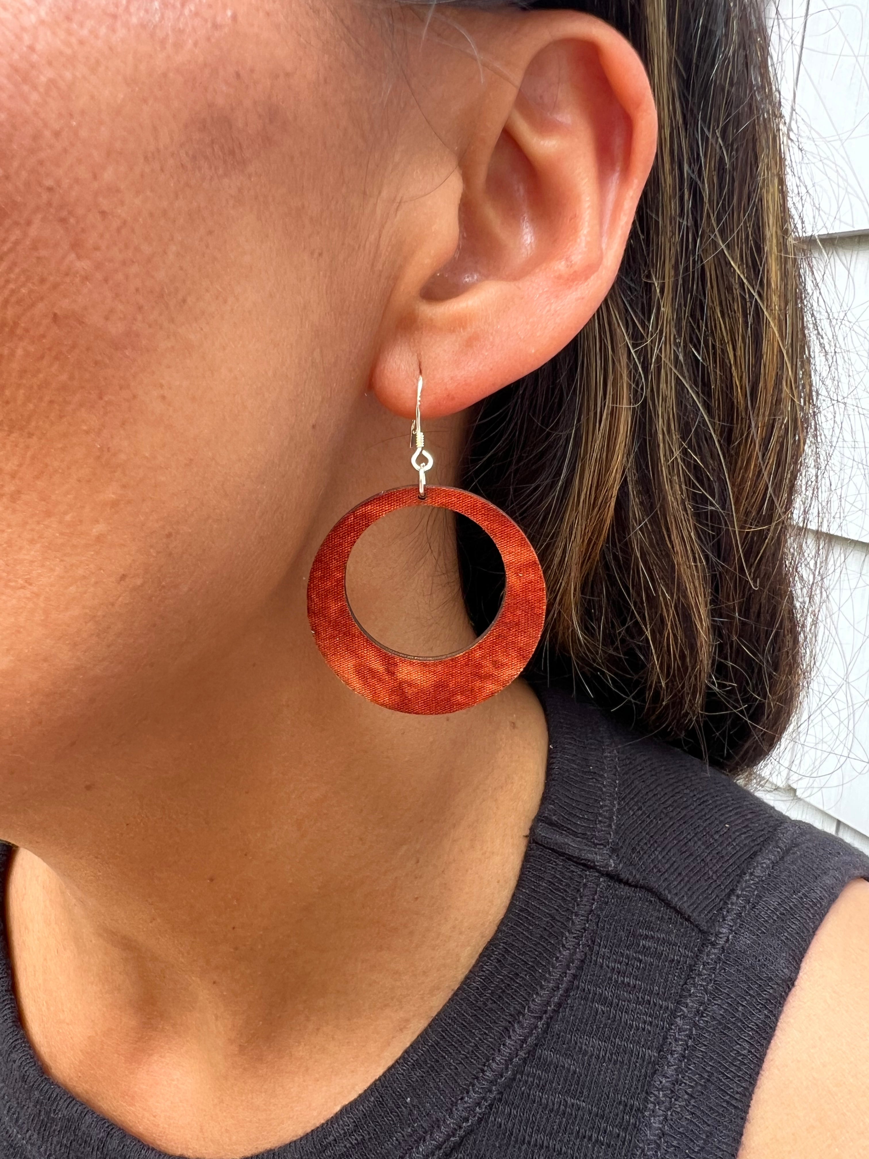 Close-up of a person wearing a cranberry wooden hoop earring.