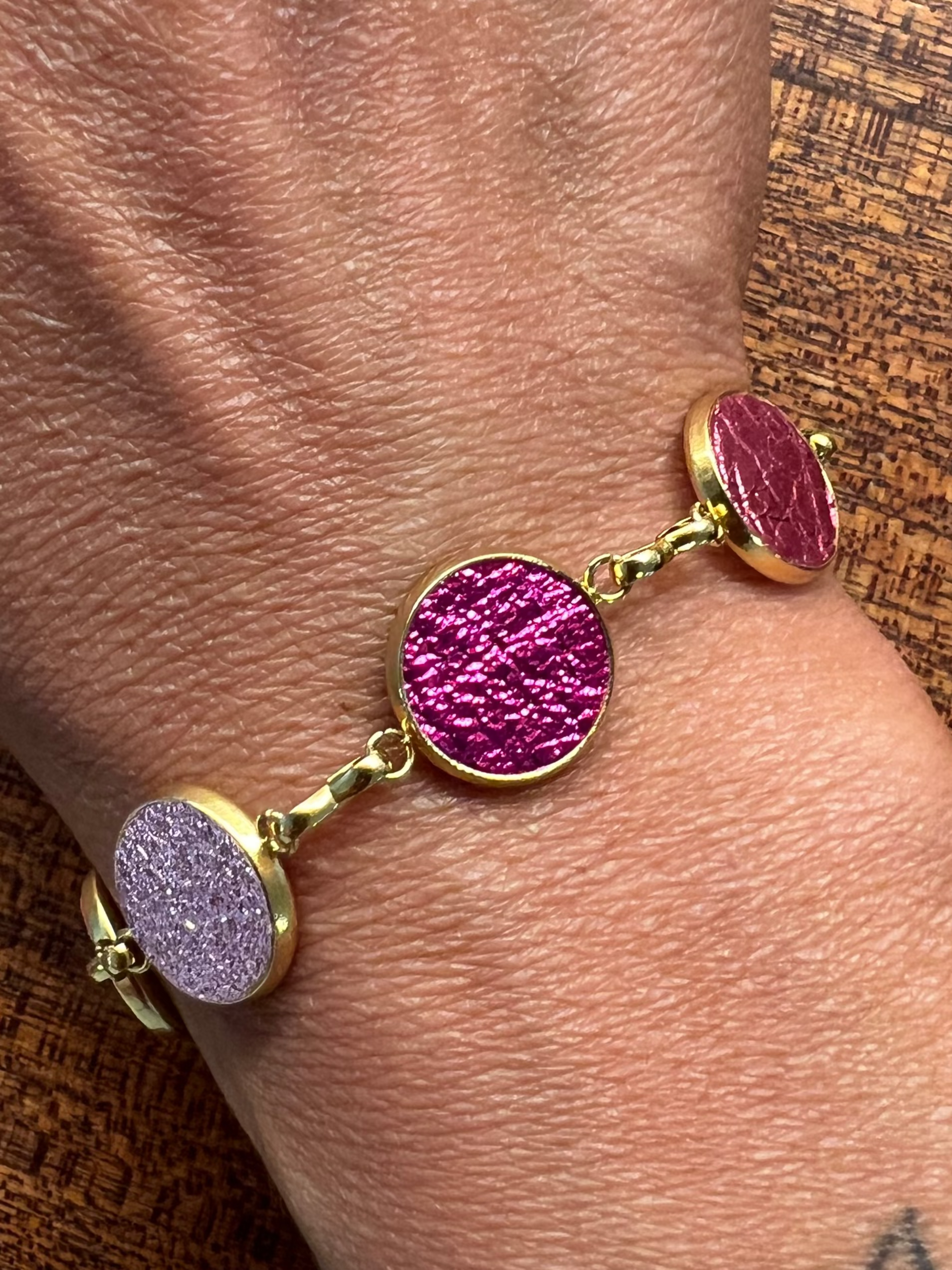 Gold Everlink bracelet in purple and pink on a wrist against a wooden background