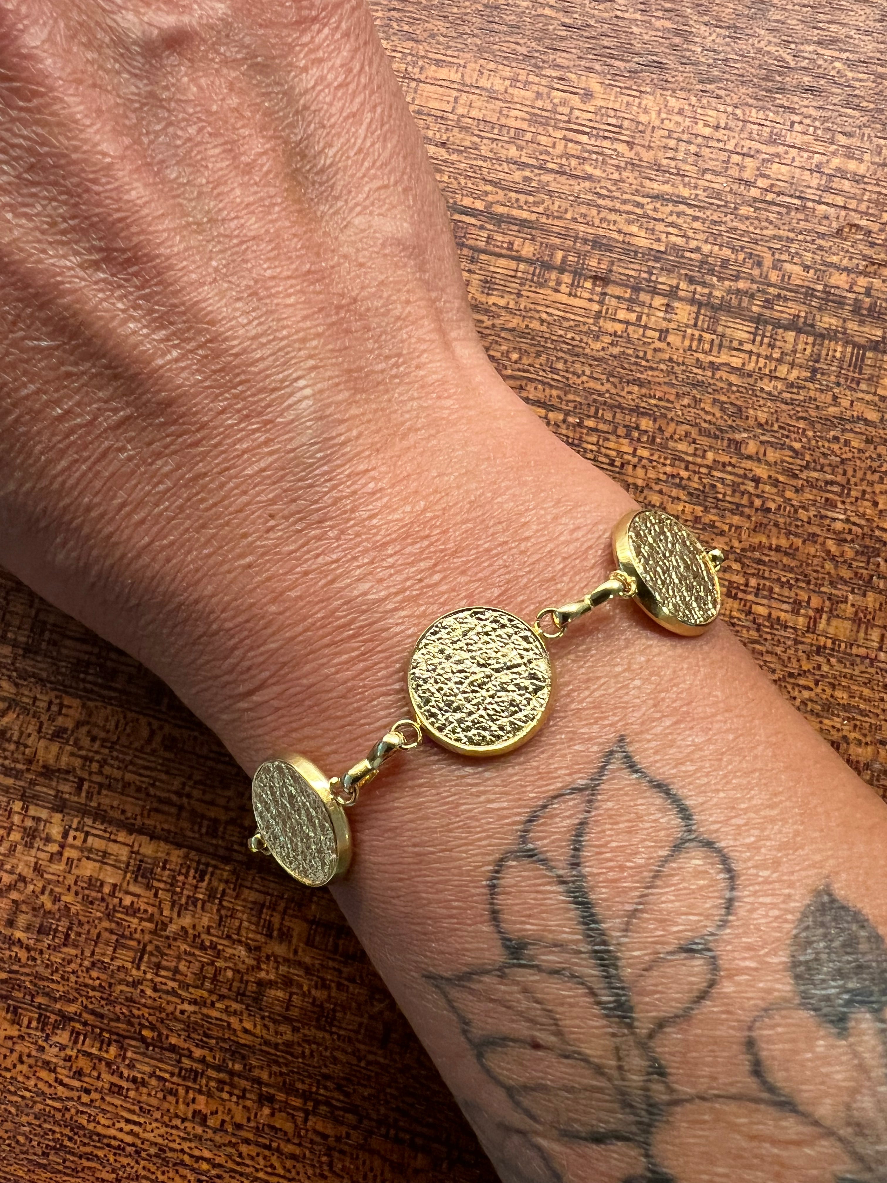 Gold bracelet on a wrist with a tattoo against a wooden background
