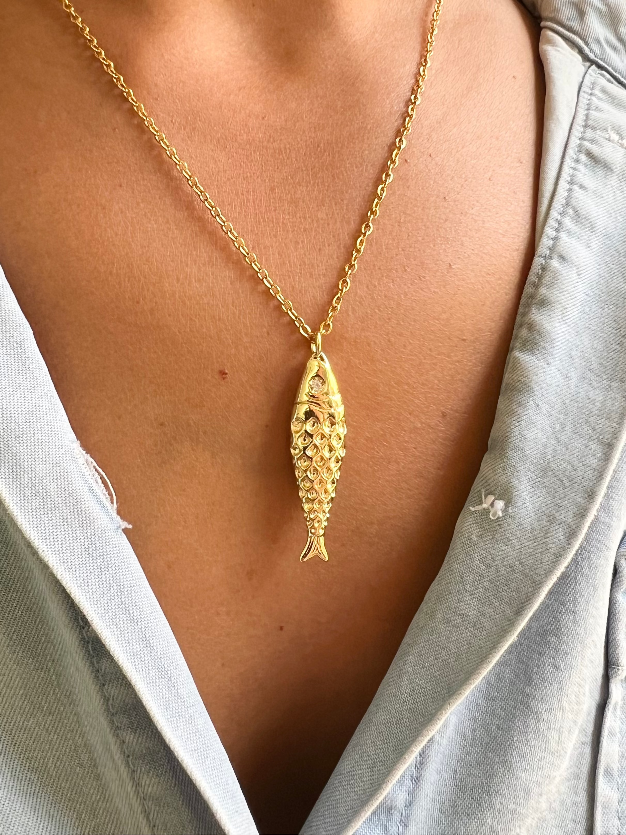 Gold necklace with a fish pendant worn by a person