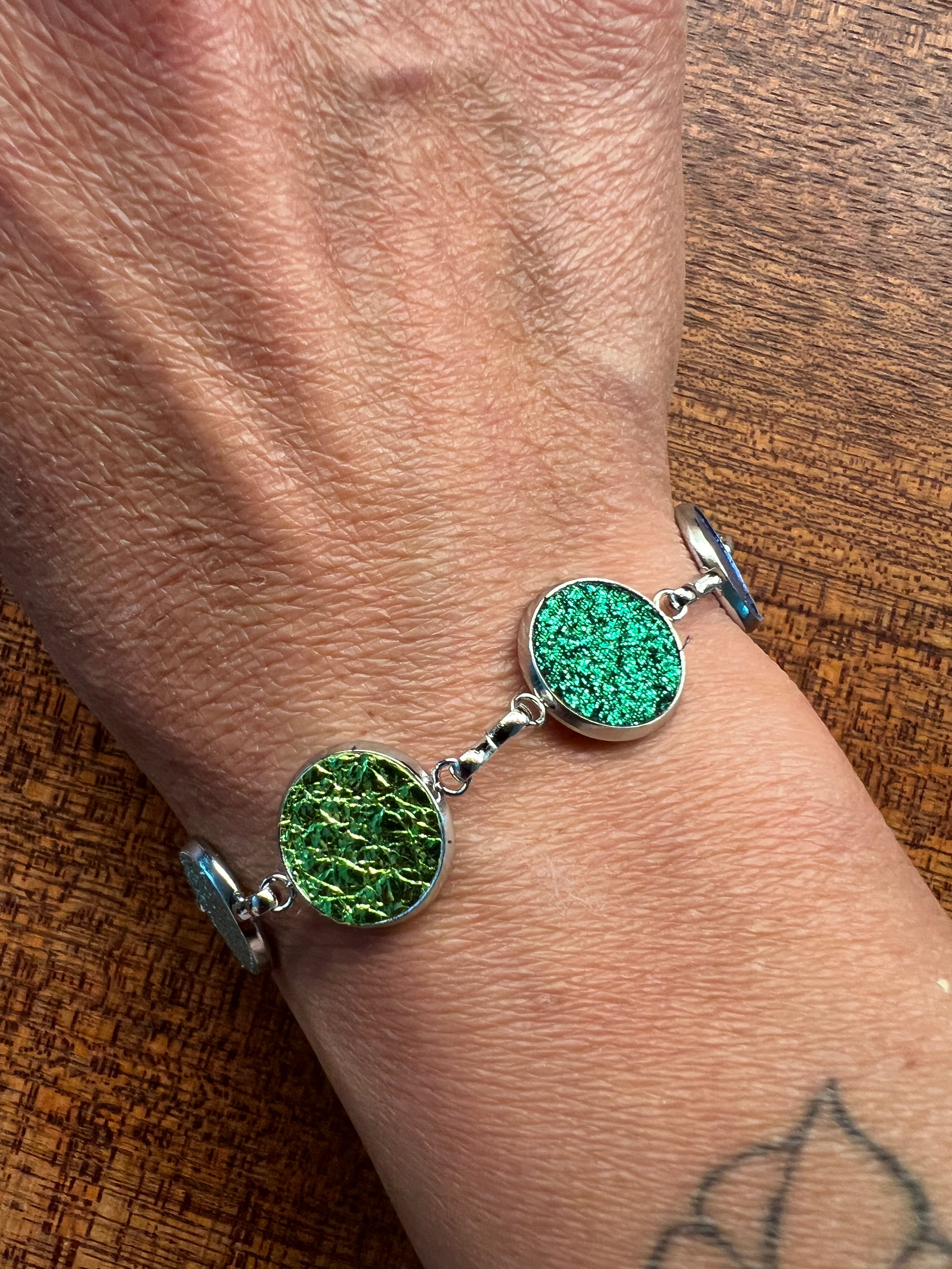 An image of a person's wrist wearing a bracelet with green leather dots and metallic hardware.