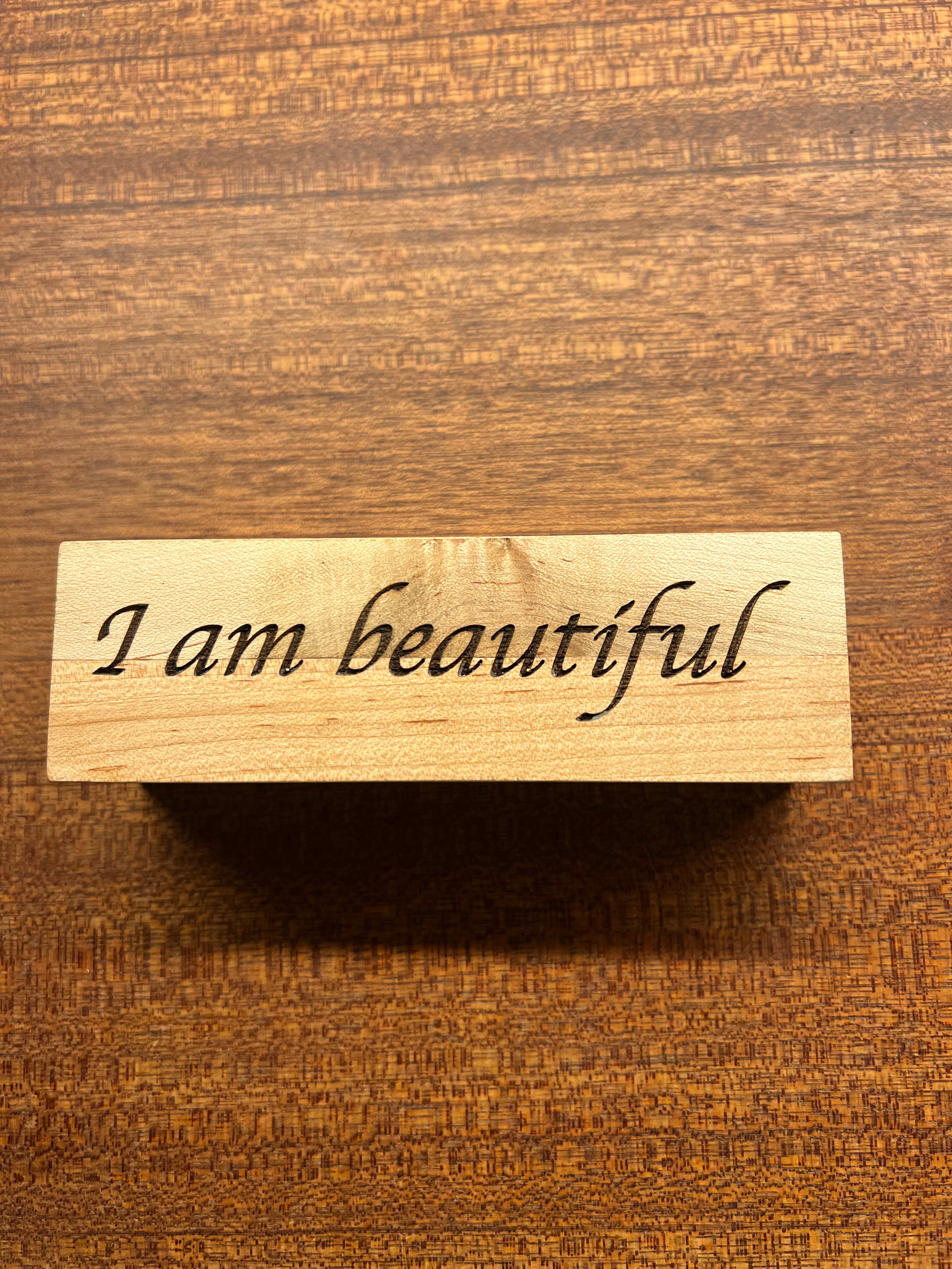 Wooden block with 'I am beautiful' engraving on a wooden surface