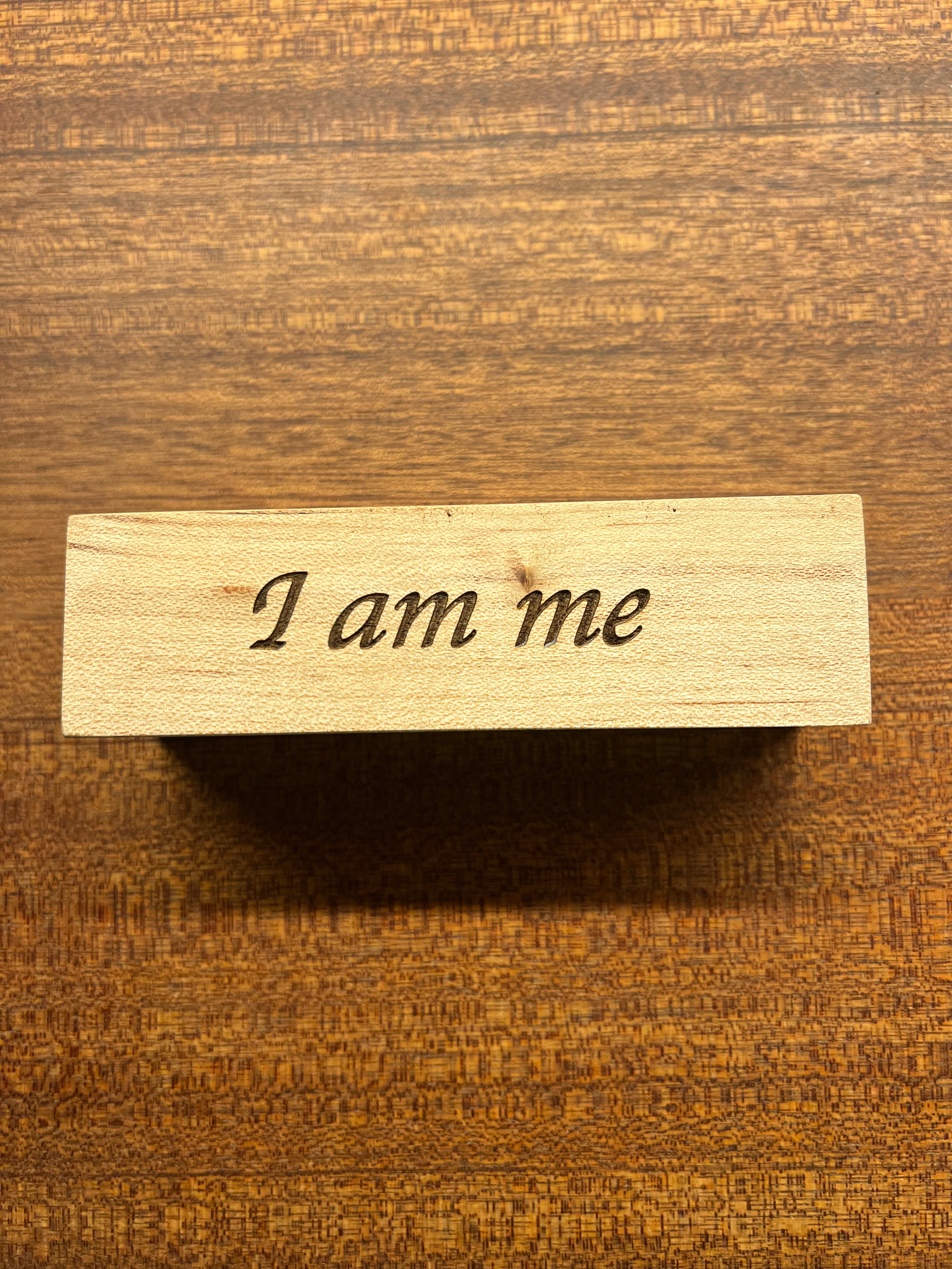 Wooden block with 'I am me' engraving on a wooden background