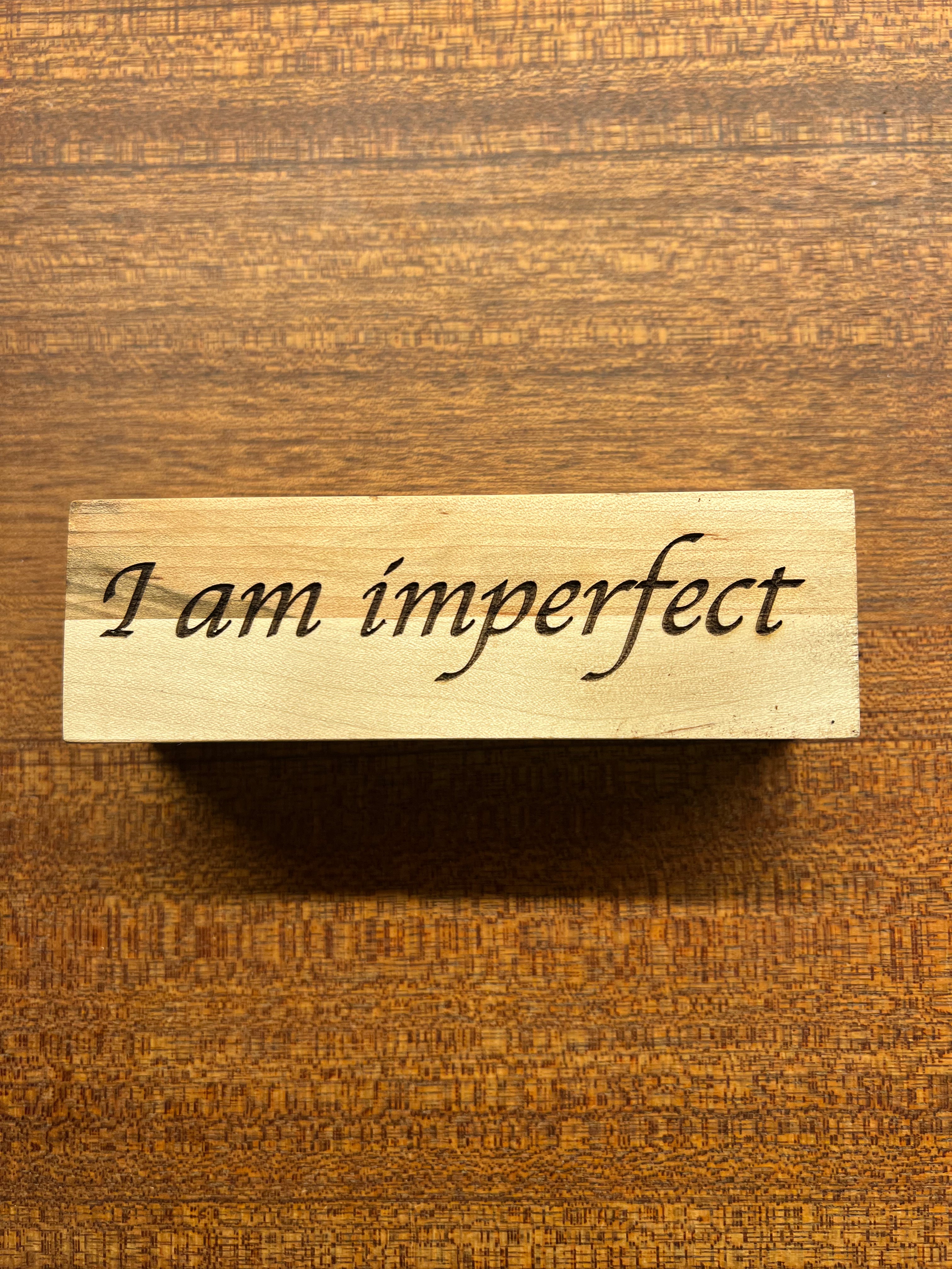 Wooden plaque with 'I am imperfect' text on a wooden background