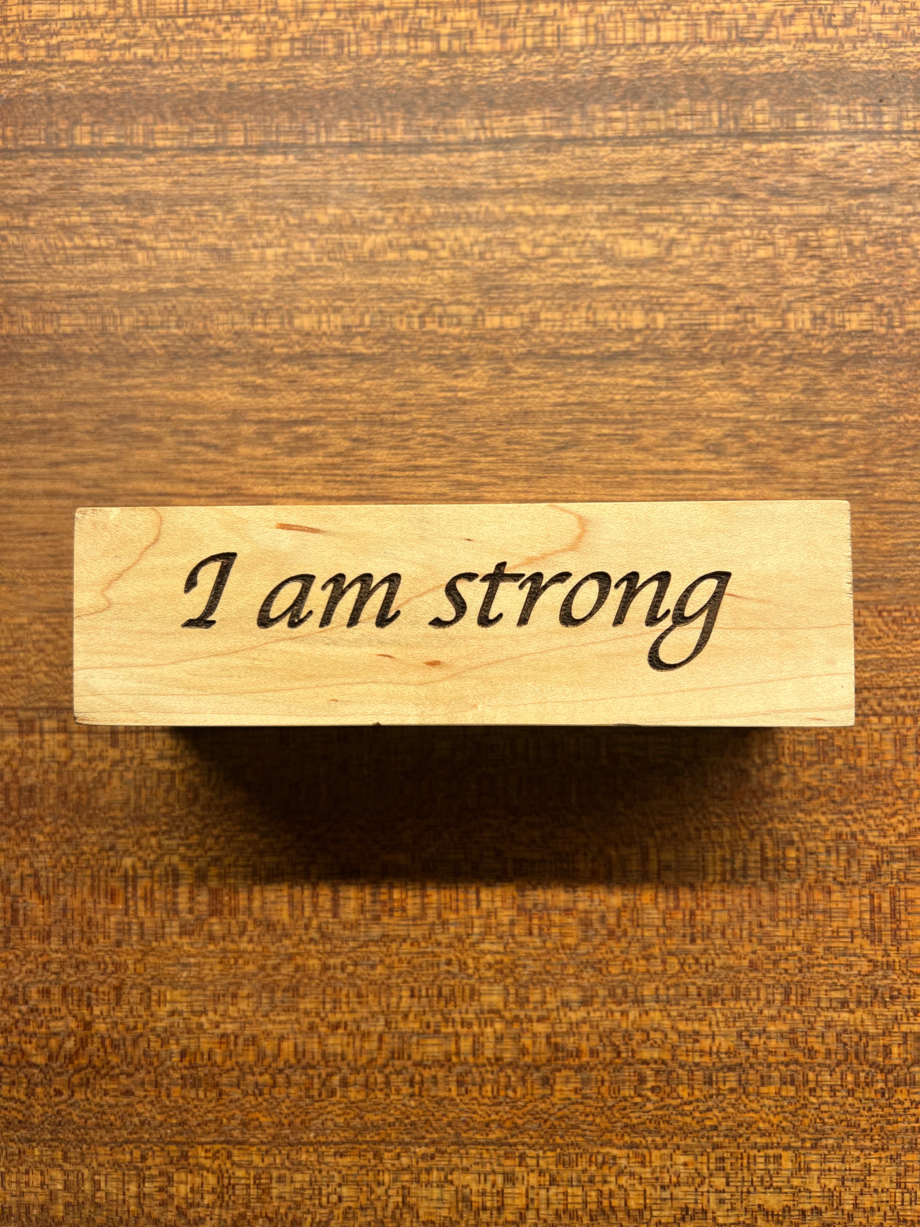 Wooden block with 'I am strong' engraving on a wooden background