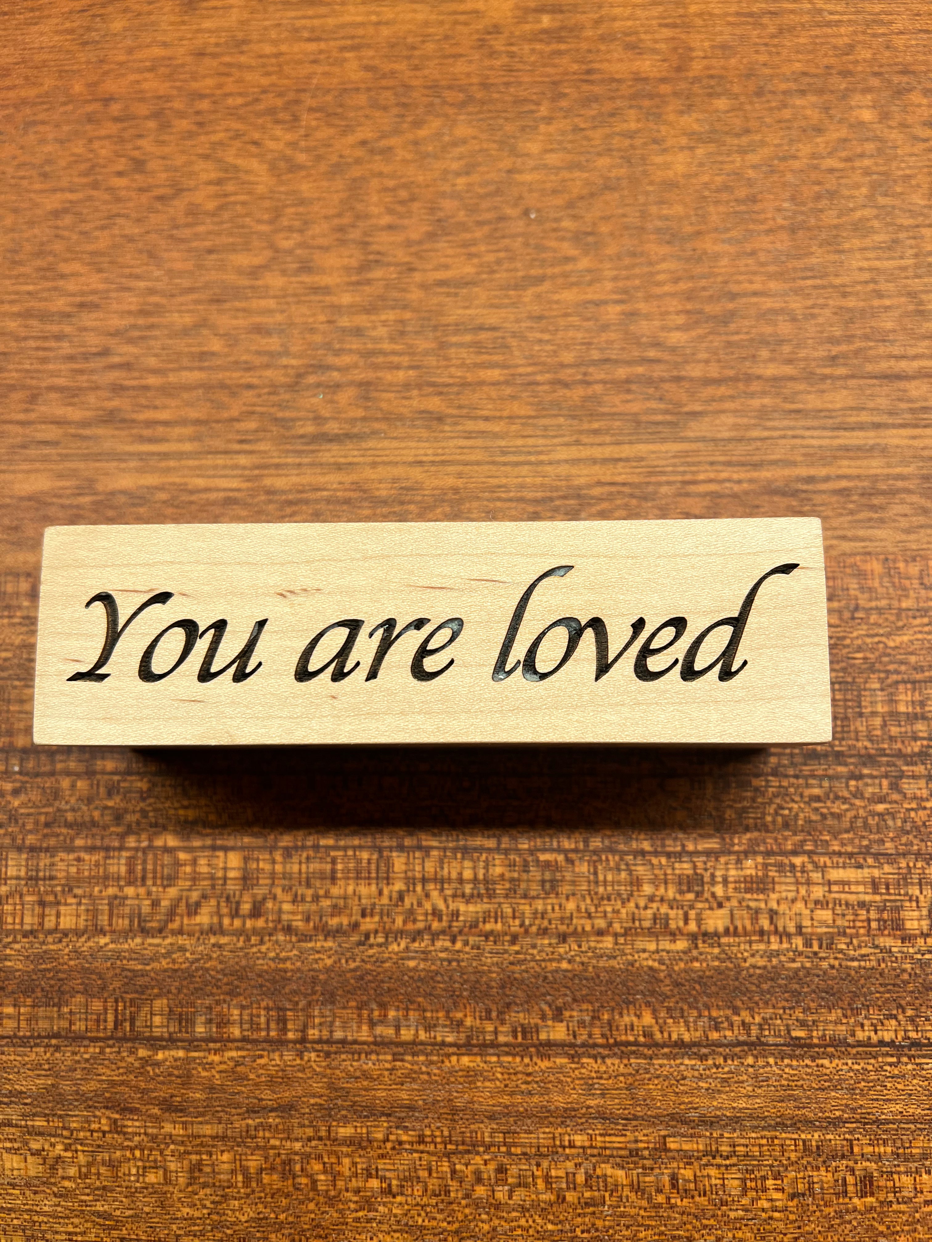 Wooden block with 'You are loved' text on a wooden background