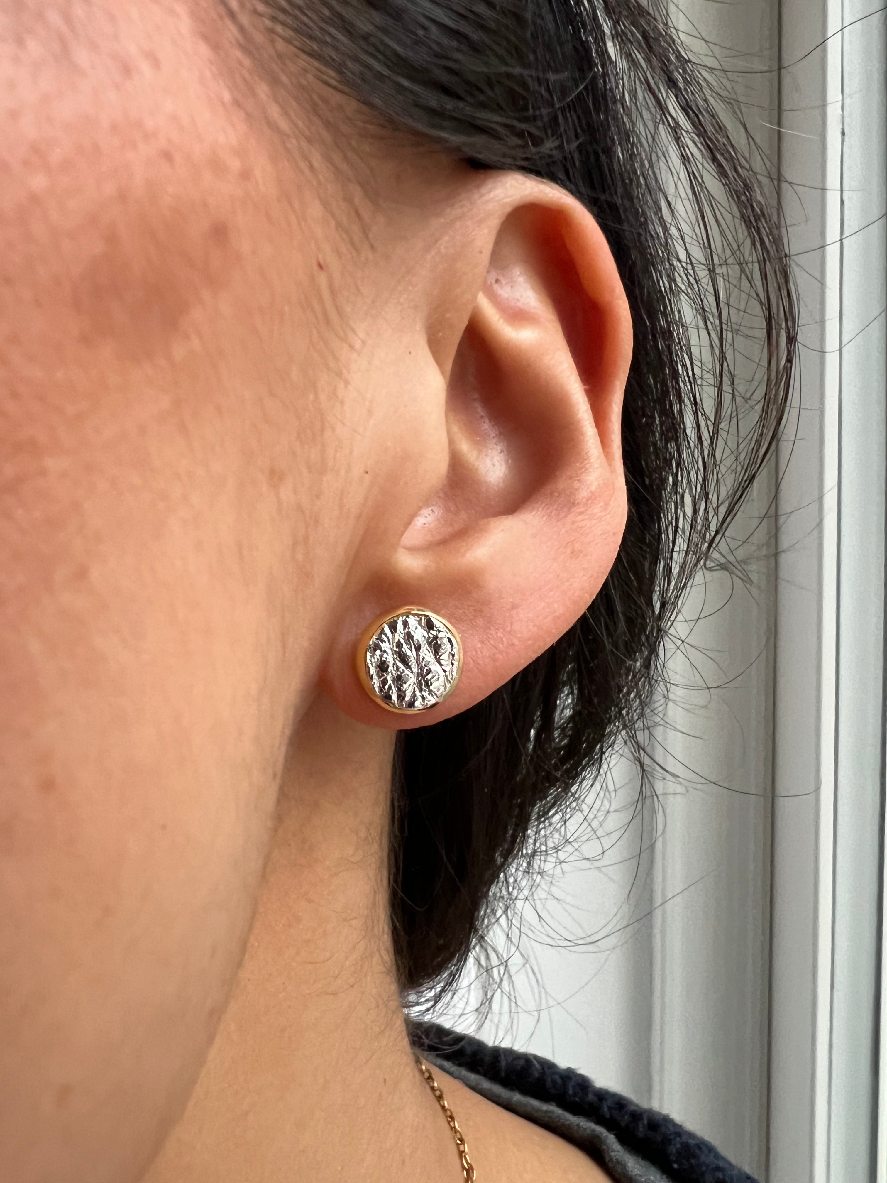 Close-up of an ear wearing a silver textured earring with a blurred background