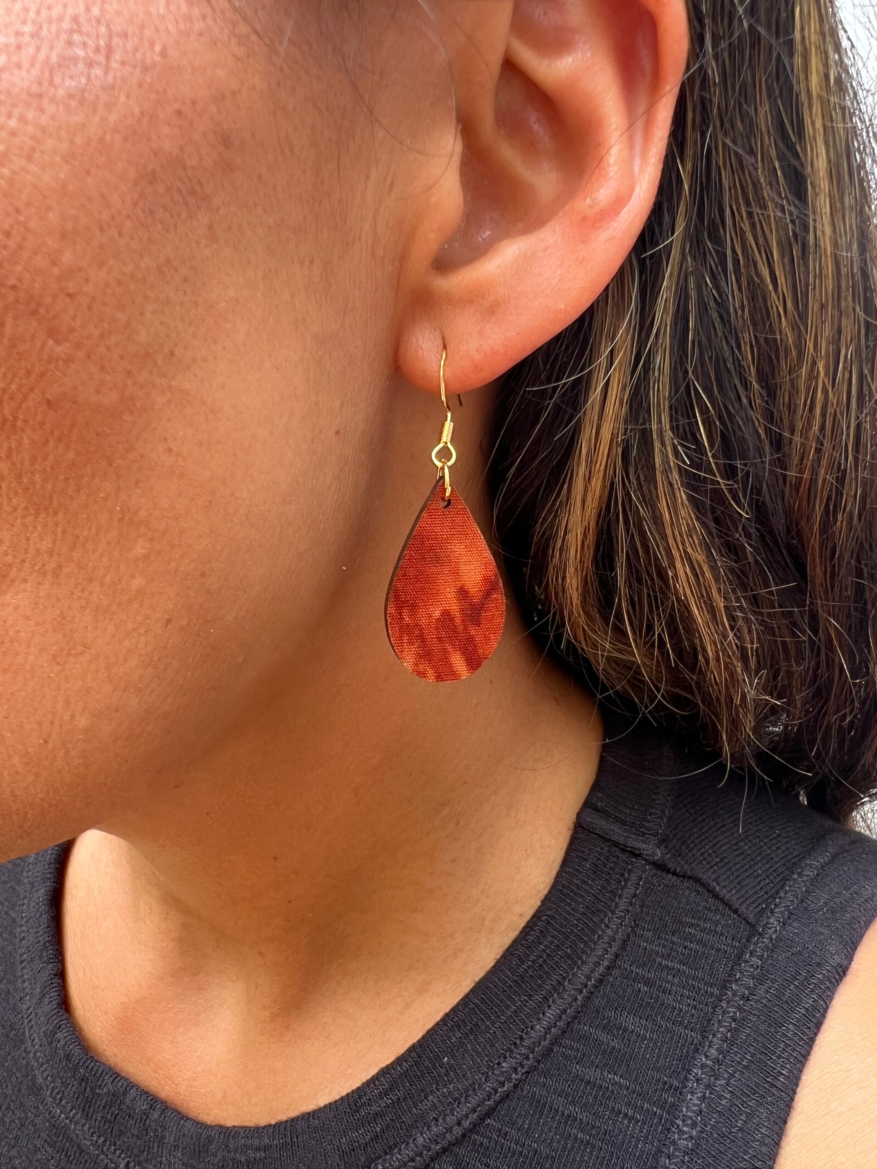 Close-up of a person wearing a brown teardrop earring with gold hook.