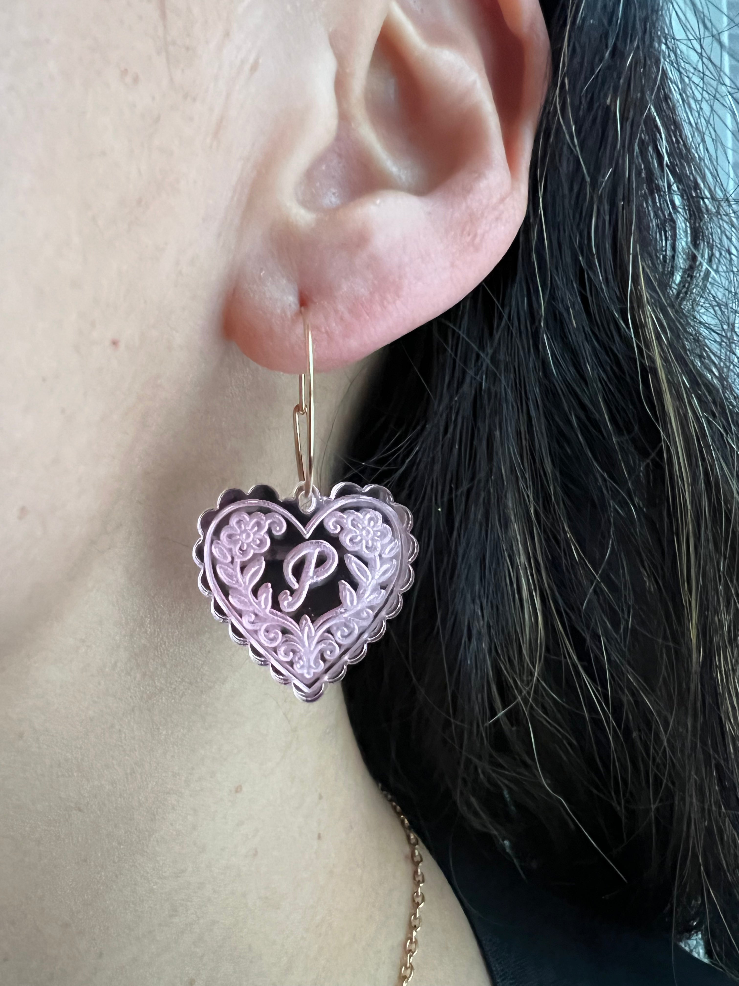 Heart-shaped earring with a letter 'P' detail worn by a person.