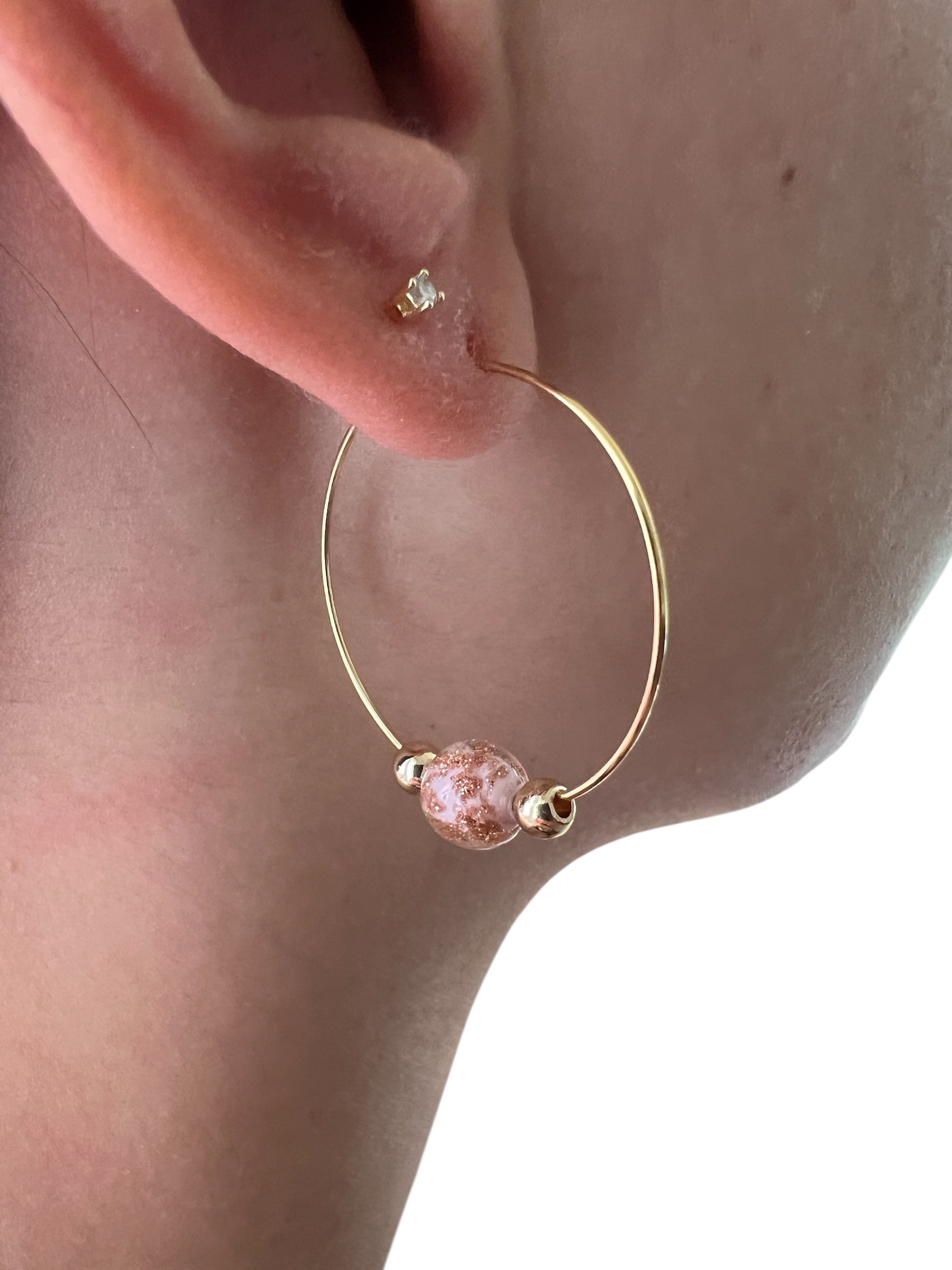 Gold hoop earring with a pink bead worn on an ear