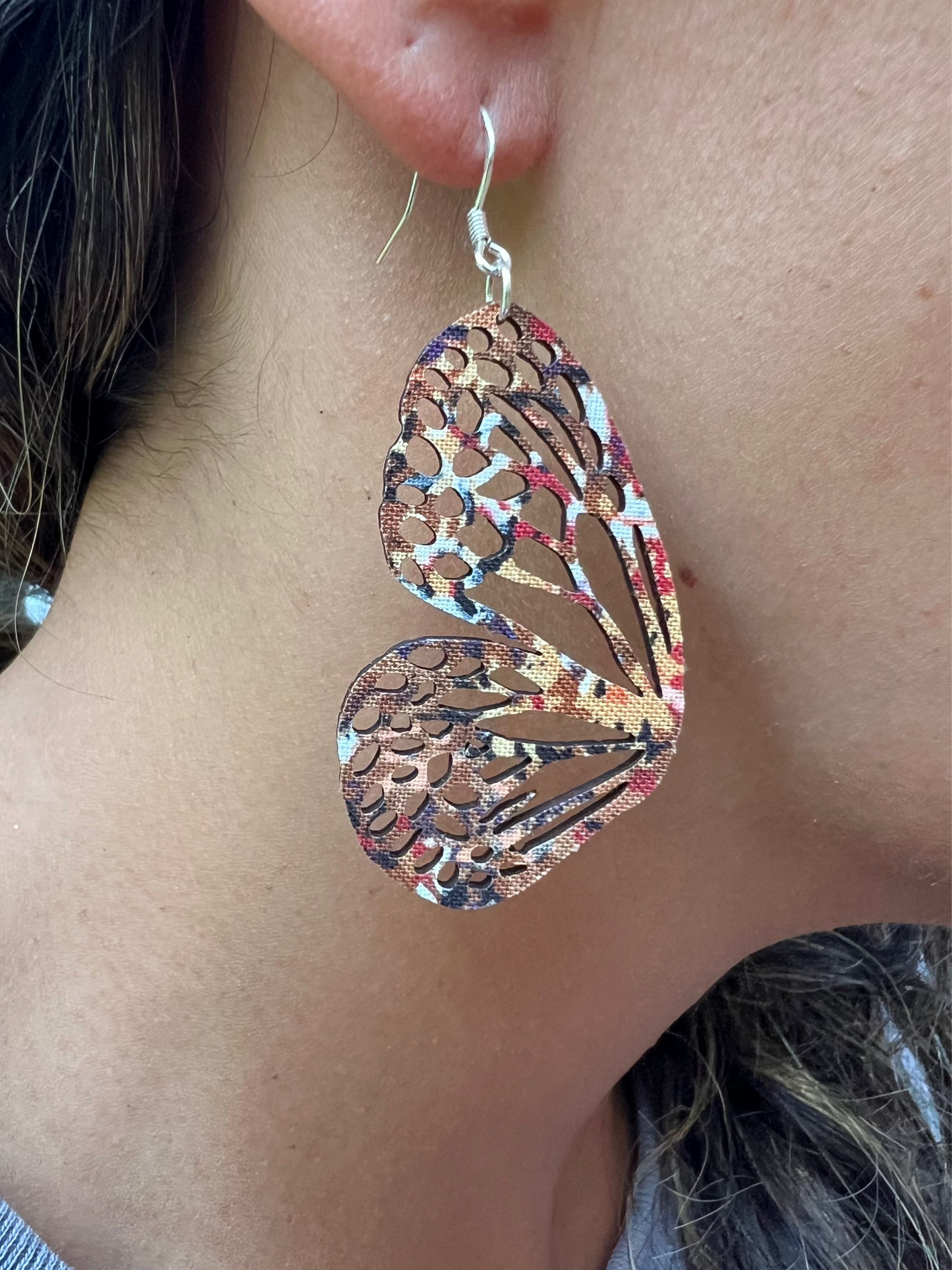 Close-up of a person wearing a pair of intricately designed butterfly wing earrings.