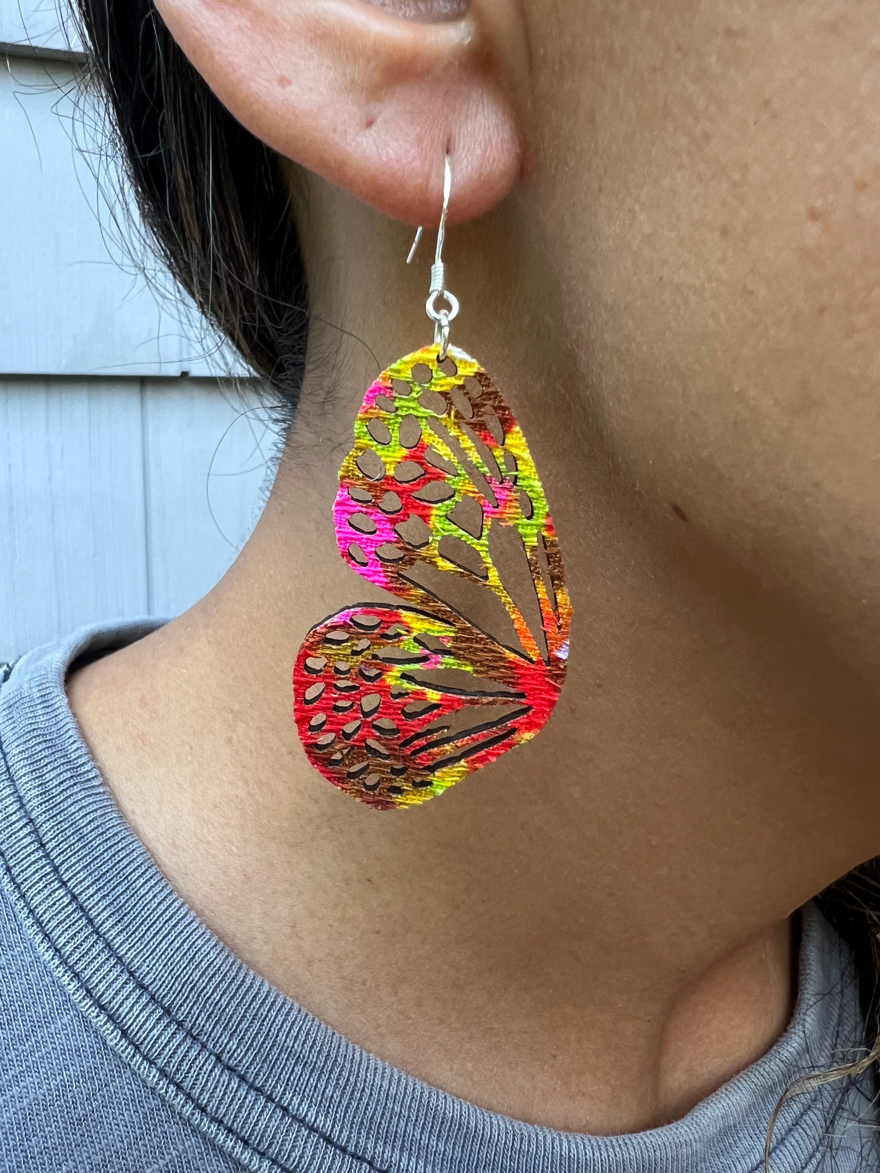 Colorful butterfly-shaped earrings worn by a person.