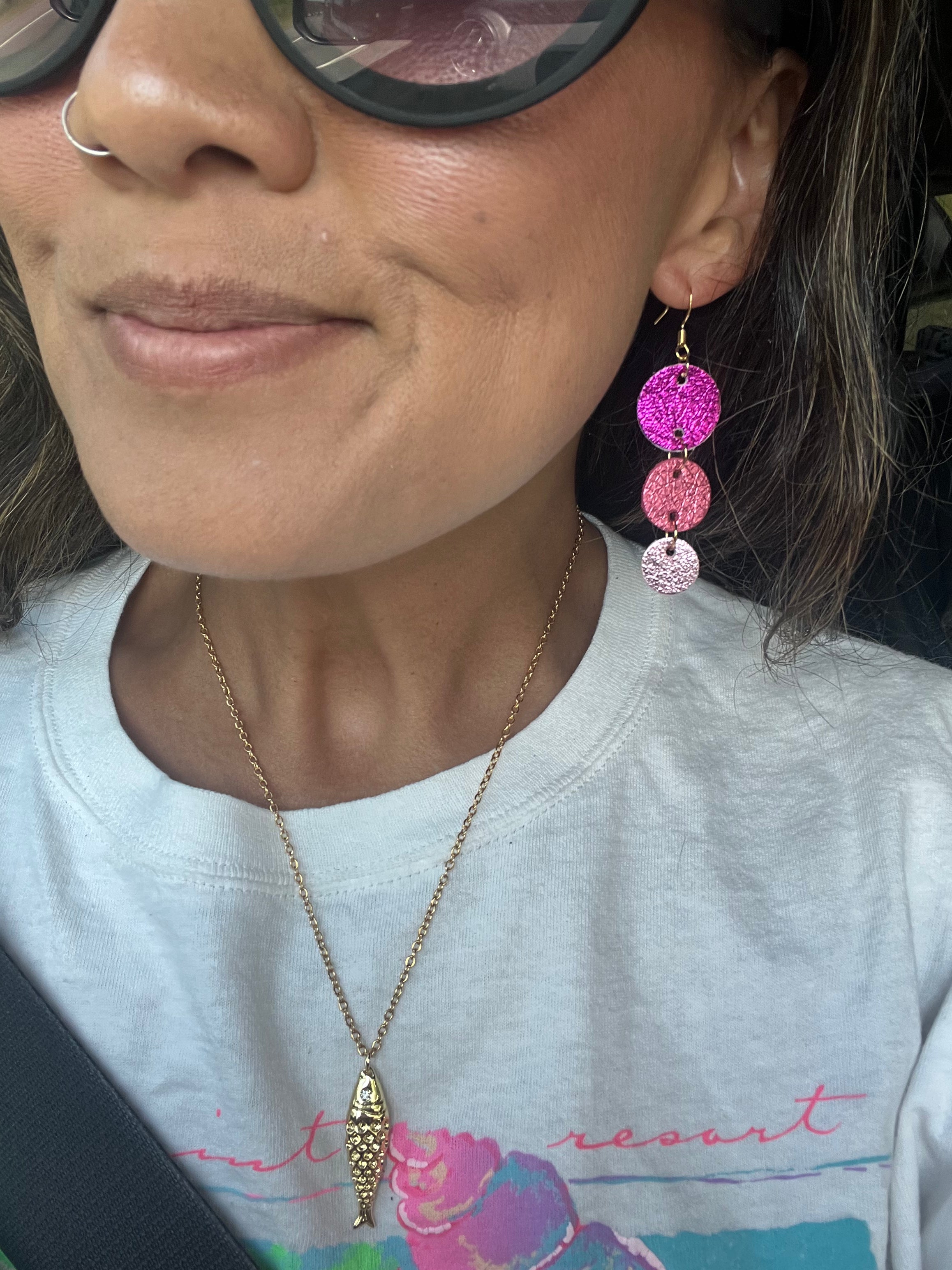 Close-up of a person wearing pink earrings and a necklace, with a blurred background.