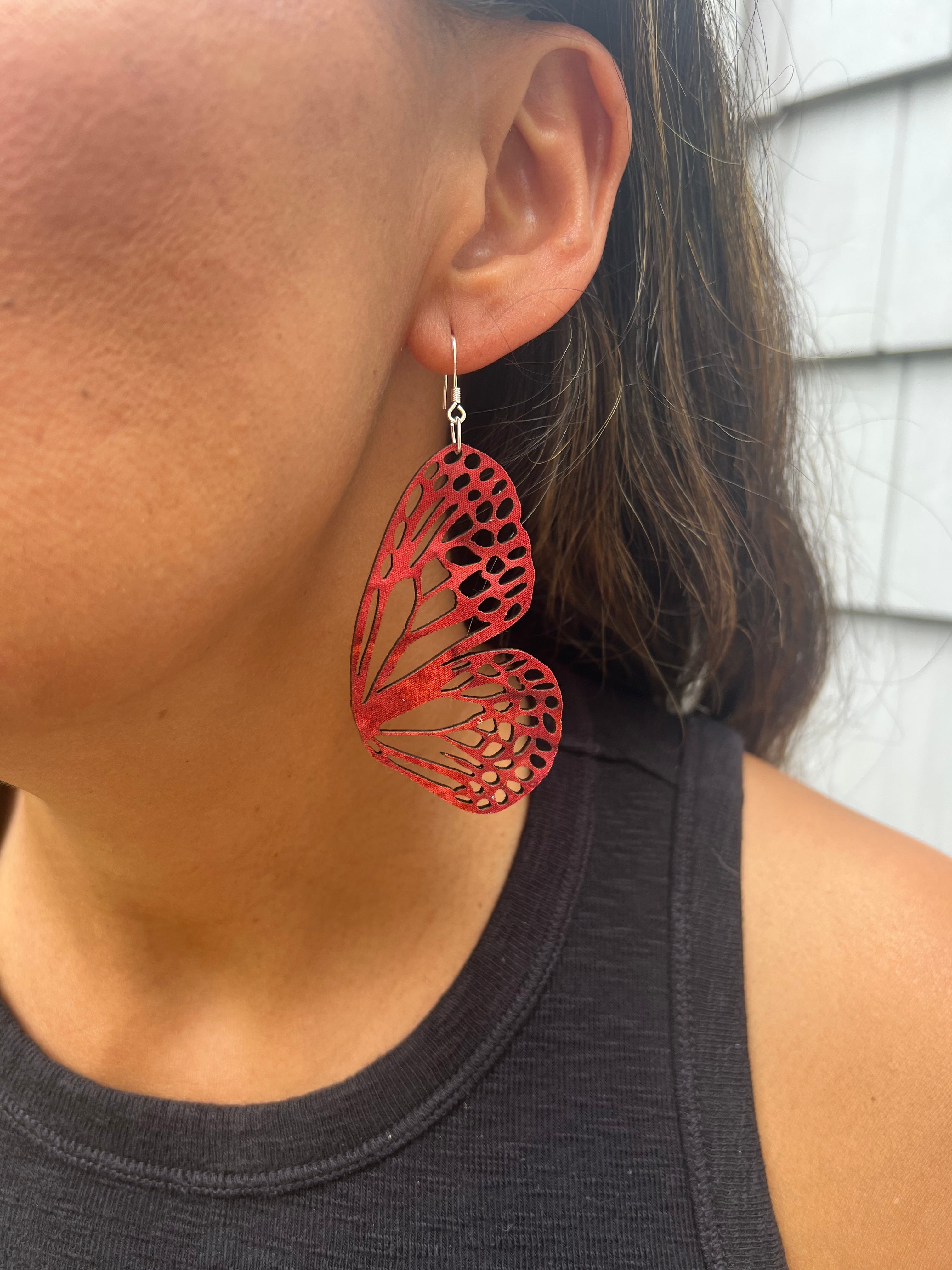 Red butterfly-shaped earrings worn by a person with a neutral background