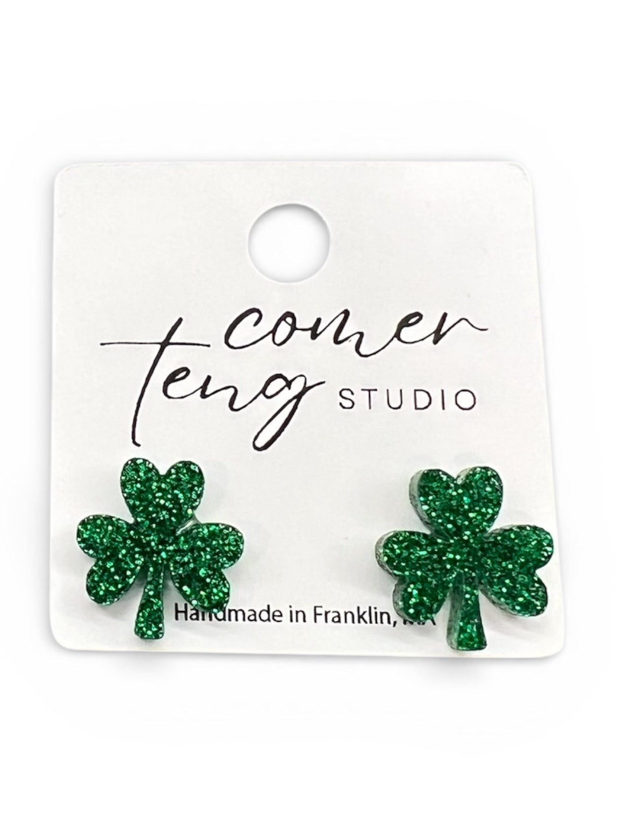 Green glitter shamrock earrings on a Cameo Teng Studio card.