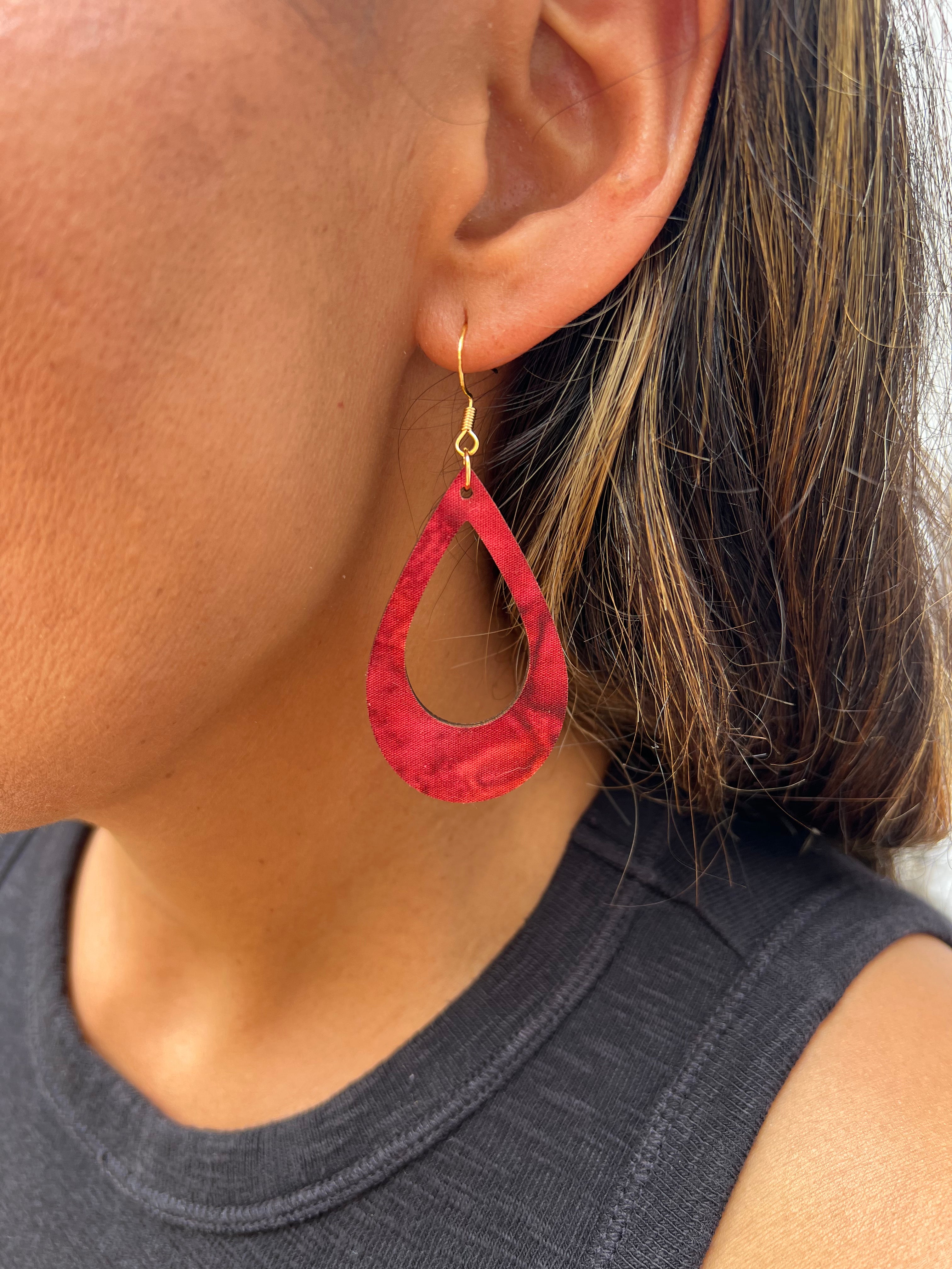 Close-up of a person wearing a red hoop earring with gold hook.