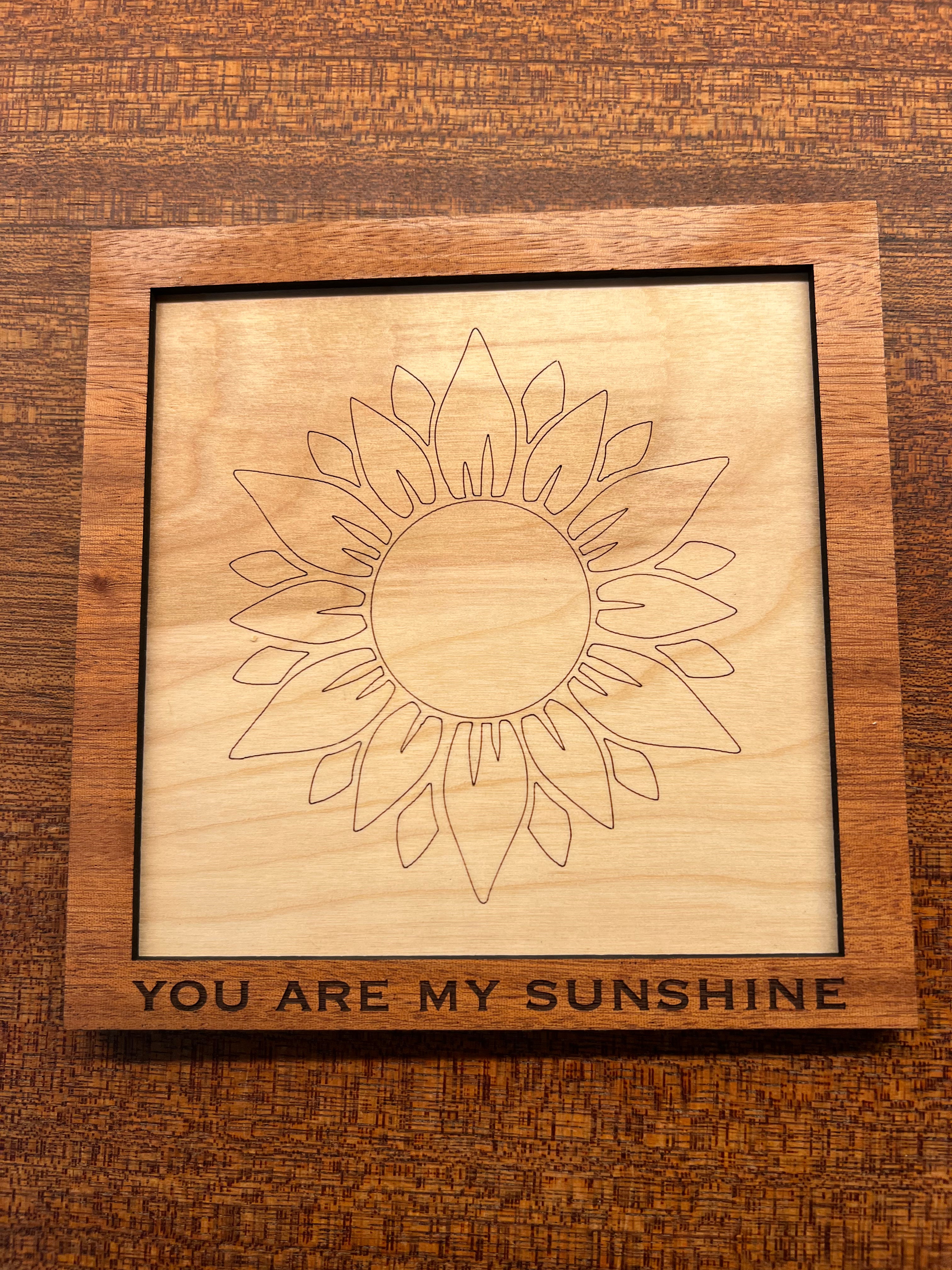 Wooden plaque with sun design and 'You Are My Sunshine' text on a wooden surface