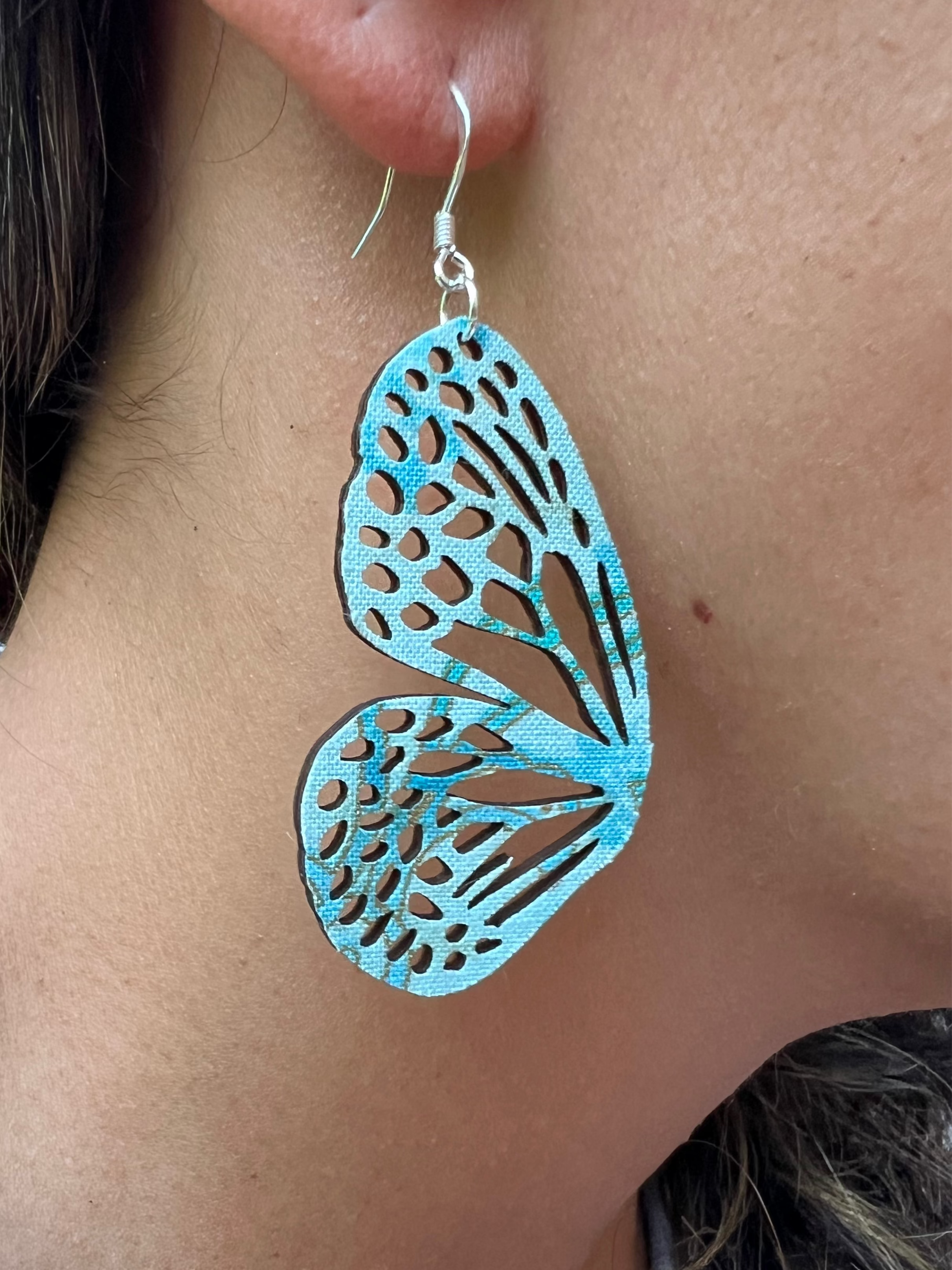 Close-up of a person wearing turquoise butterfly-shaped earrings.