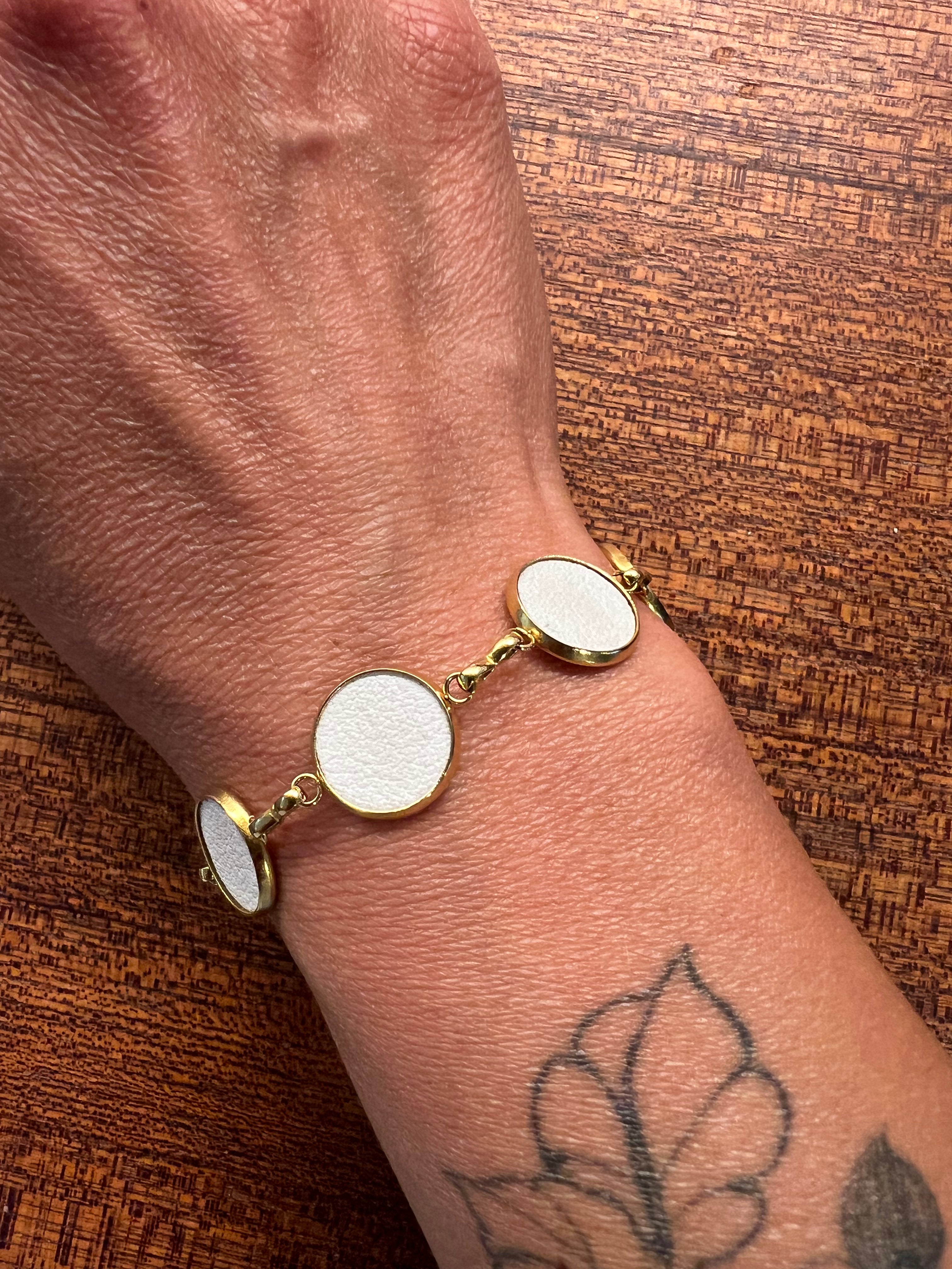 Gold Everlink  bracelet with white on a wrist against a wooden background