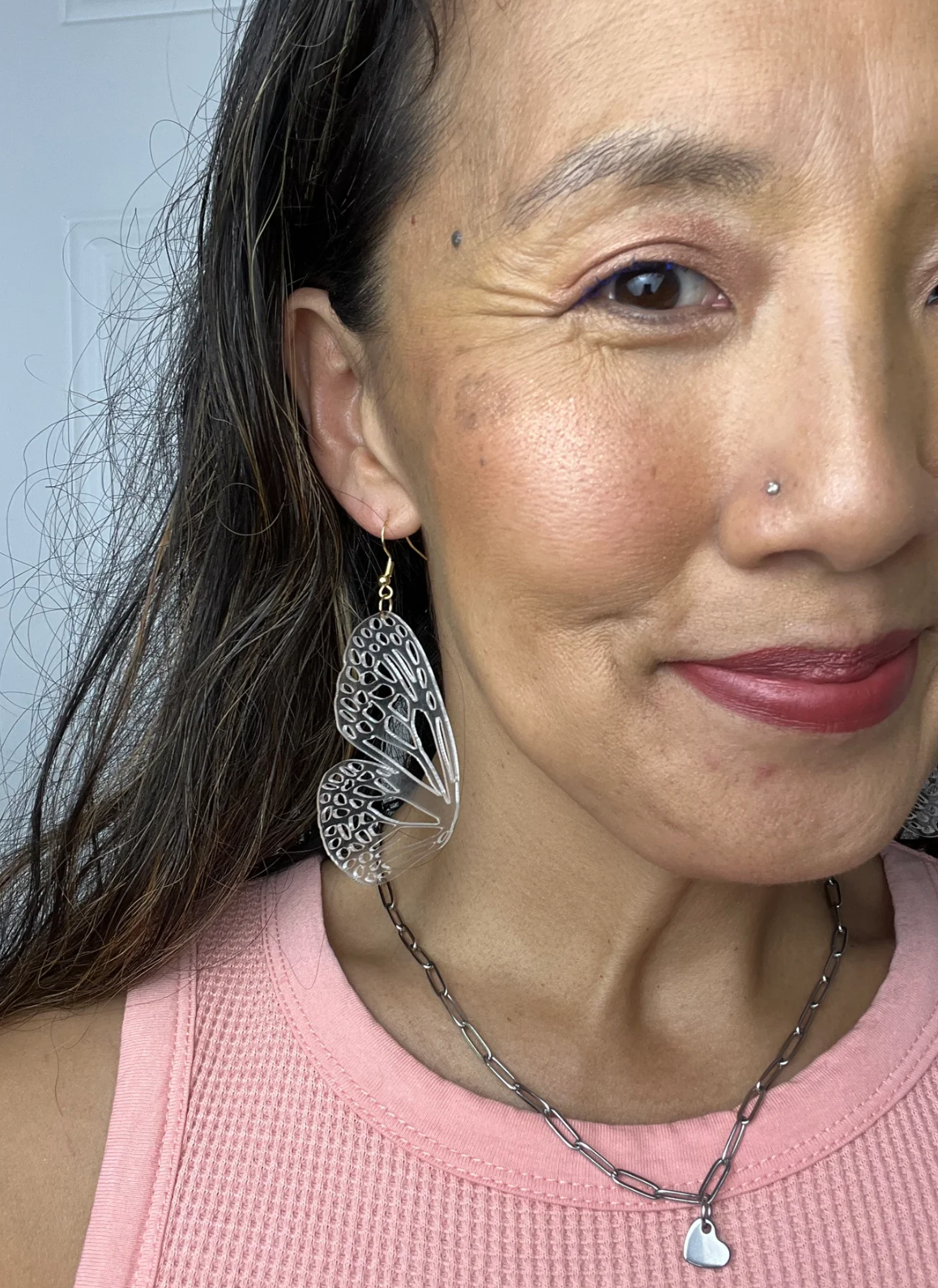 Close-up of a woman wearing a pink top and clear butterfly wing earrings.