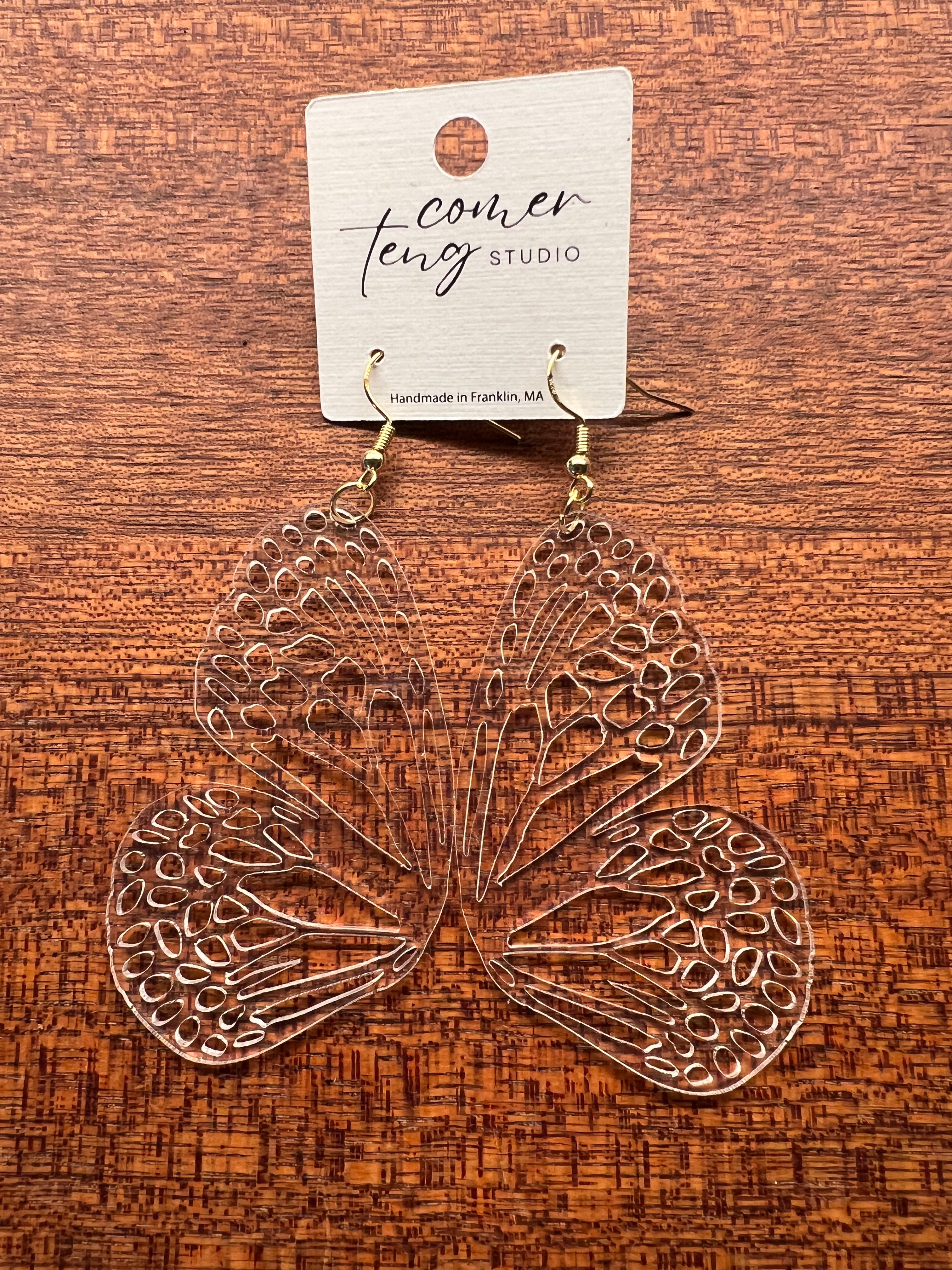 Butterfly-shaped earrings on a wooden surface with a visible brand tag.