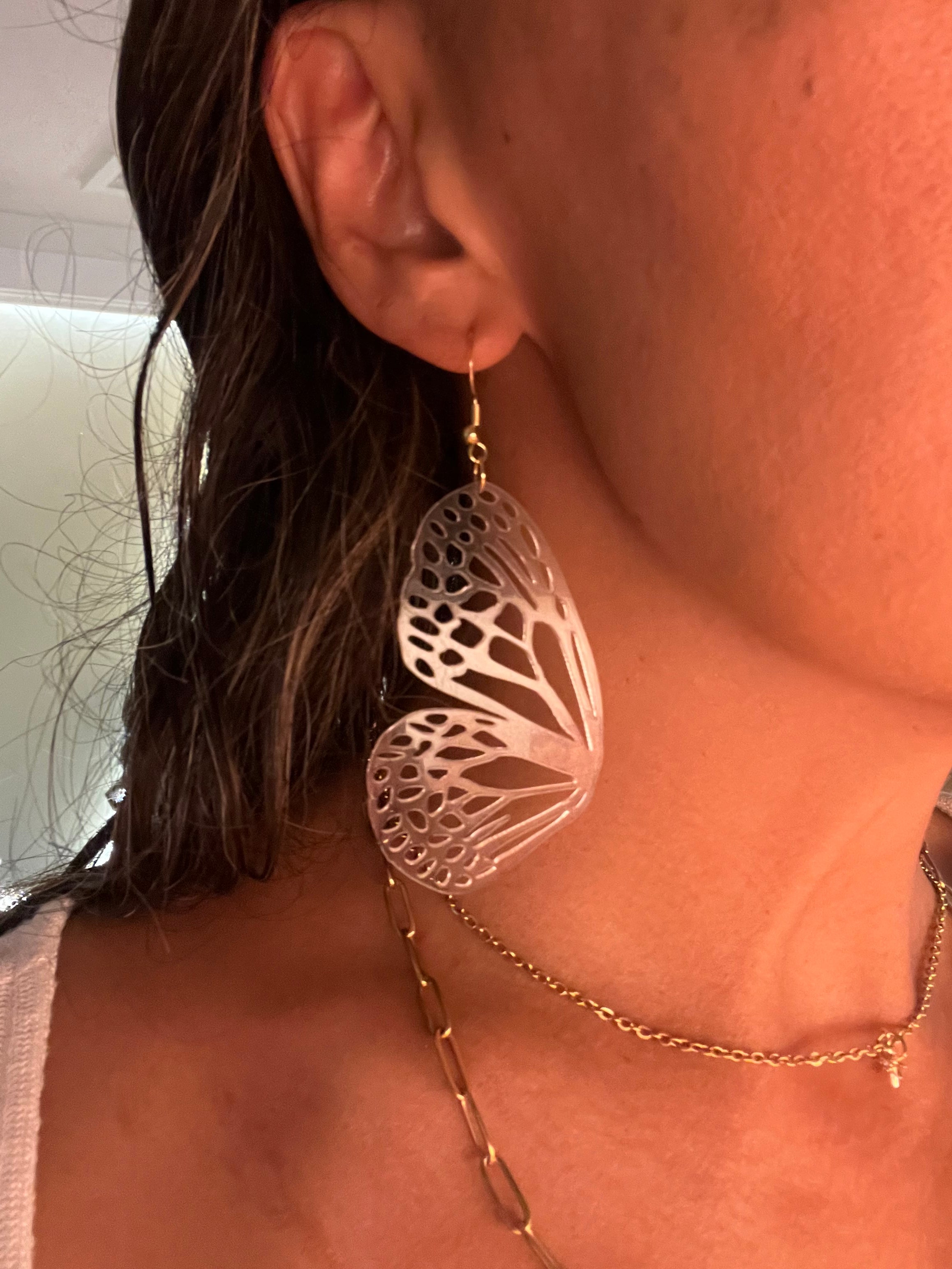 Close-up of a person wearing a delicate gold necklace with a butterfly earring.